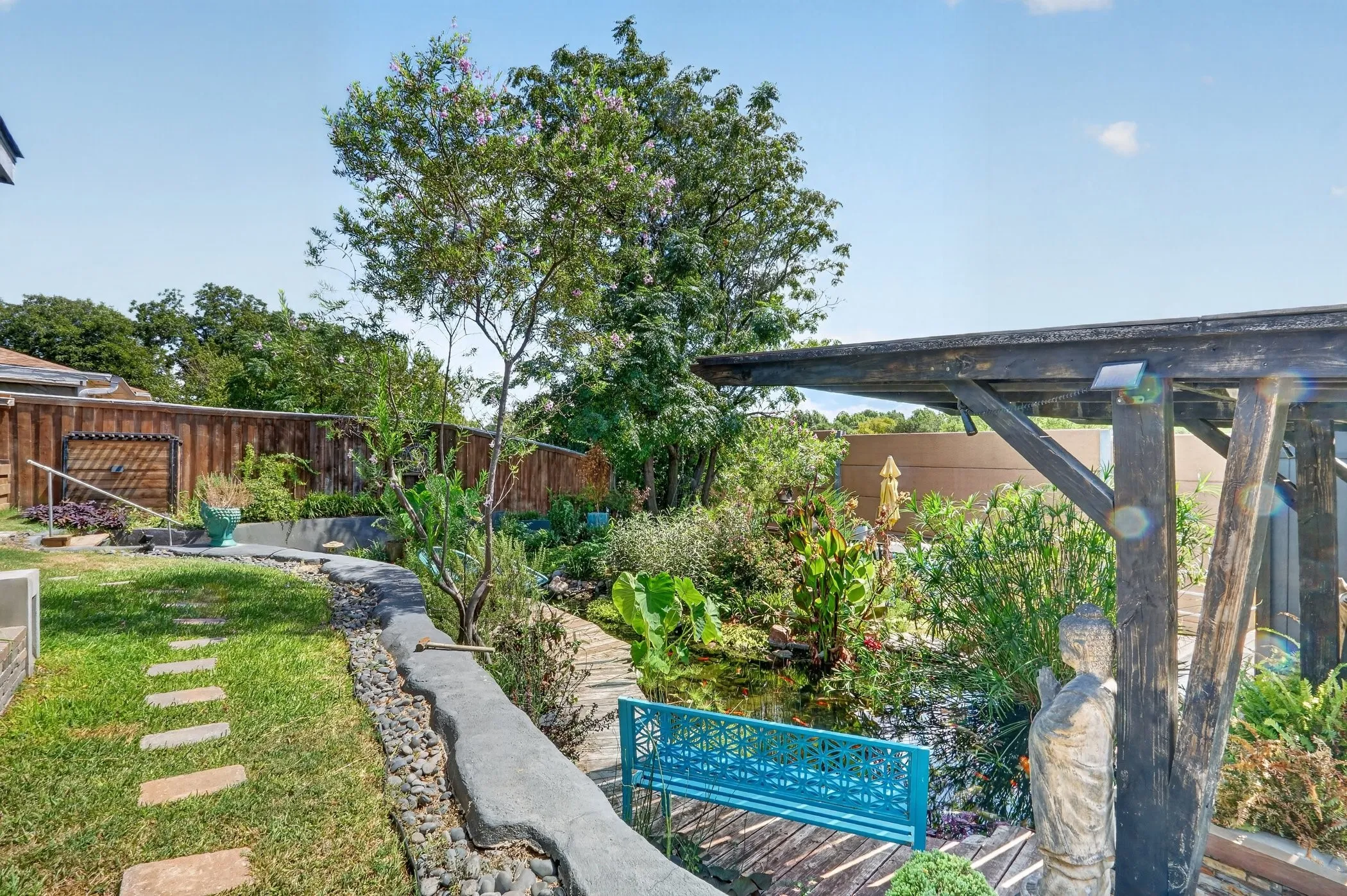 Landscaped backyard featuring a stone path, wooden fence, pergola, and decorative pond