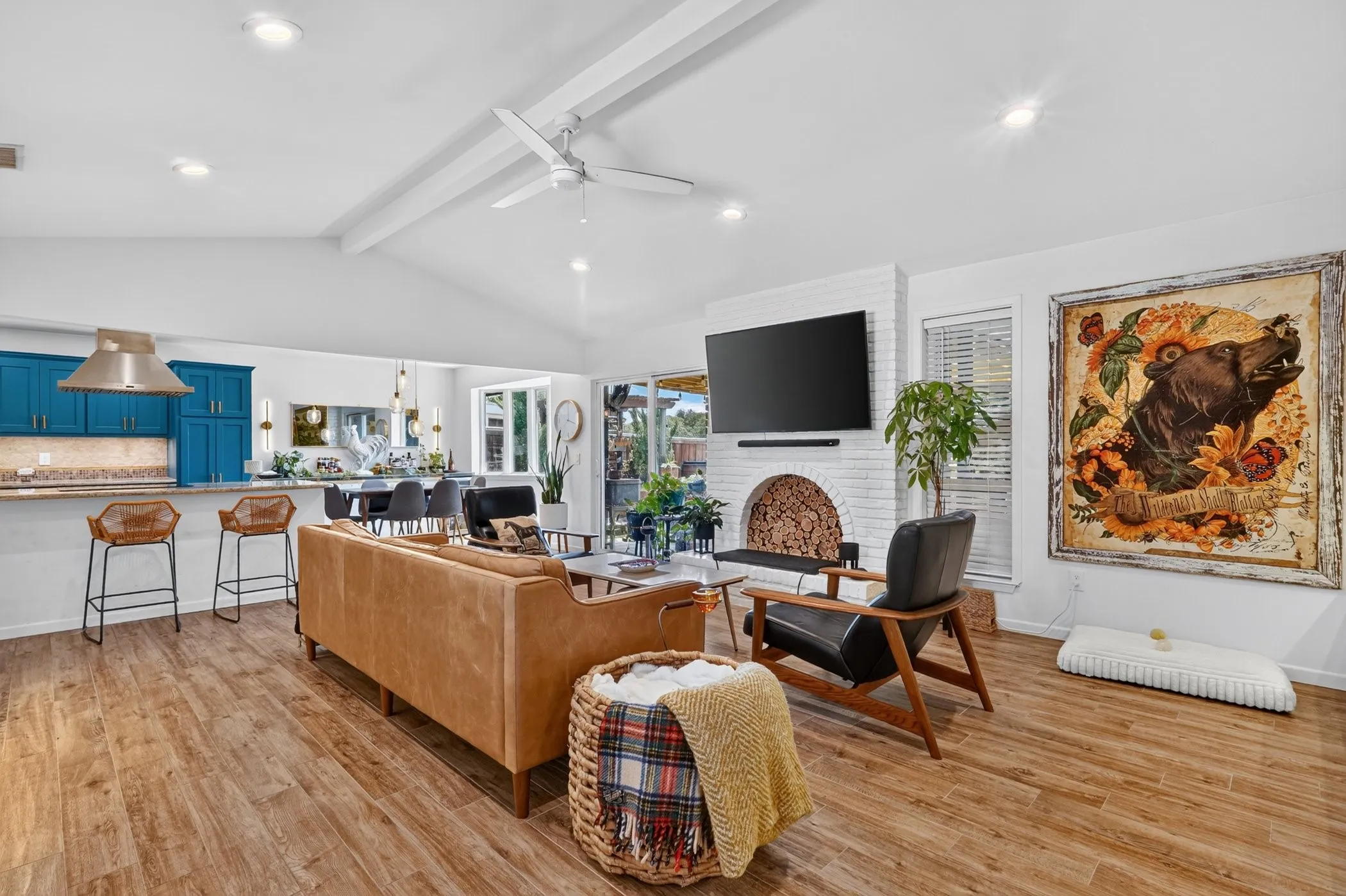 Expansive open-concept living space with vaulted ceilings, wood-finish flooring, and a white brick fireplace