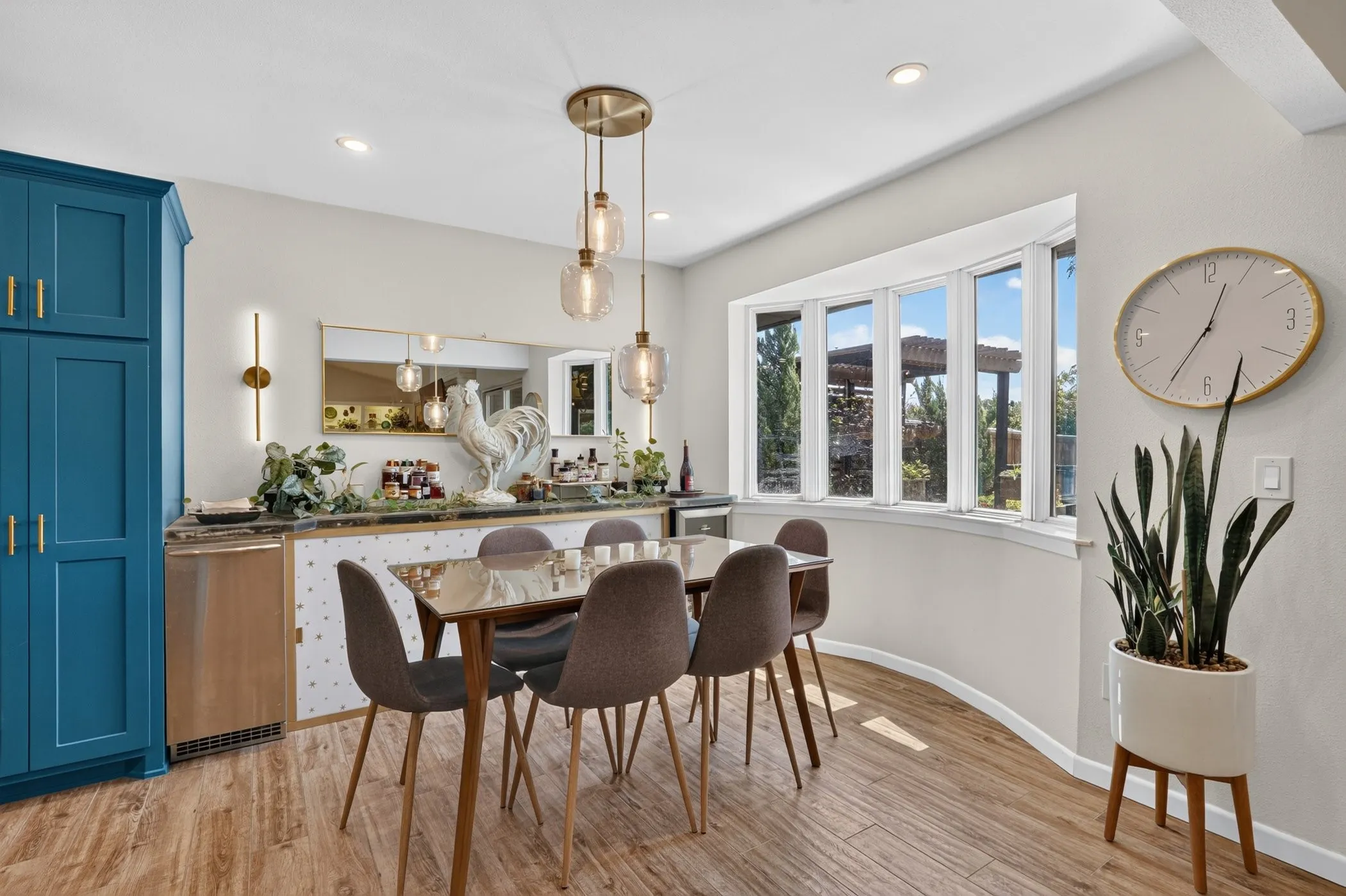 Built-in cabinetry in a vibrant blue finish, wood-finish flooring, a contemporary three-light pendant fixture, a built-in beverage refrigerator, and a curved bay window