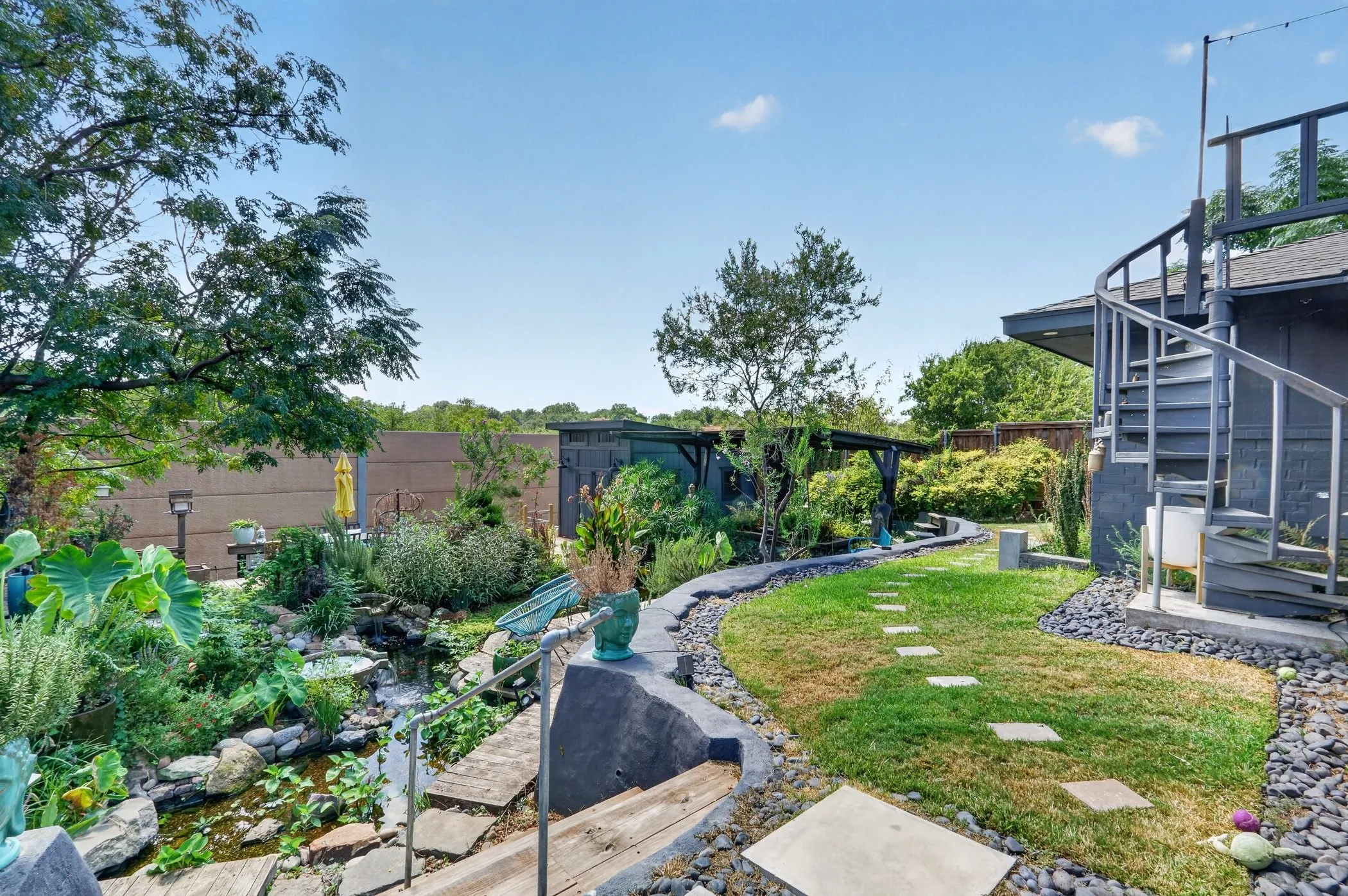 Expansive backyard featuring a spiral staircase, established landscaping, decorative gravel, and stepping stones