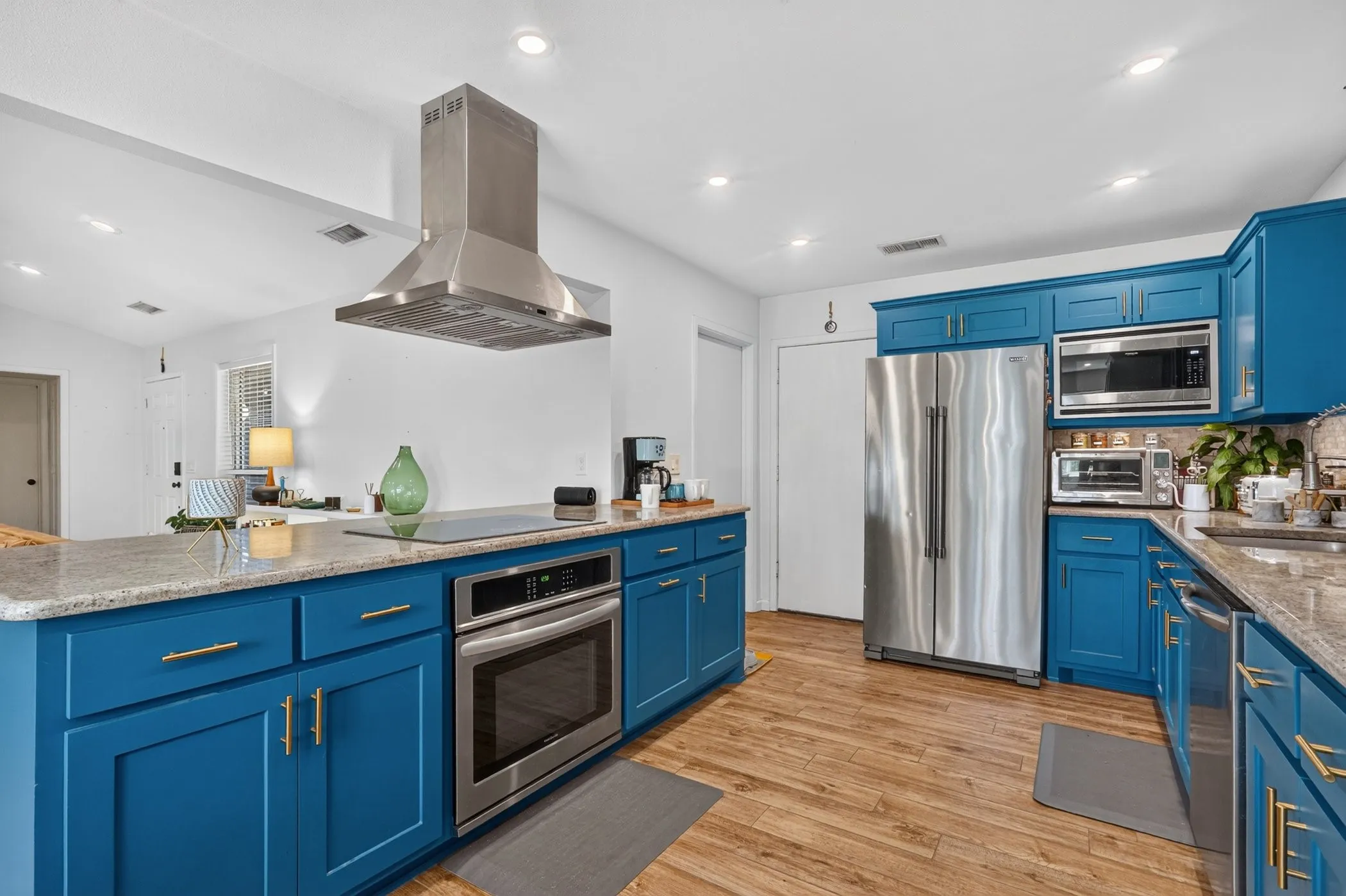 Kitchen featuring wood-finish flooring, blue cabinetry, light-toned countertops, stainless steel appliances, and a range hood