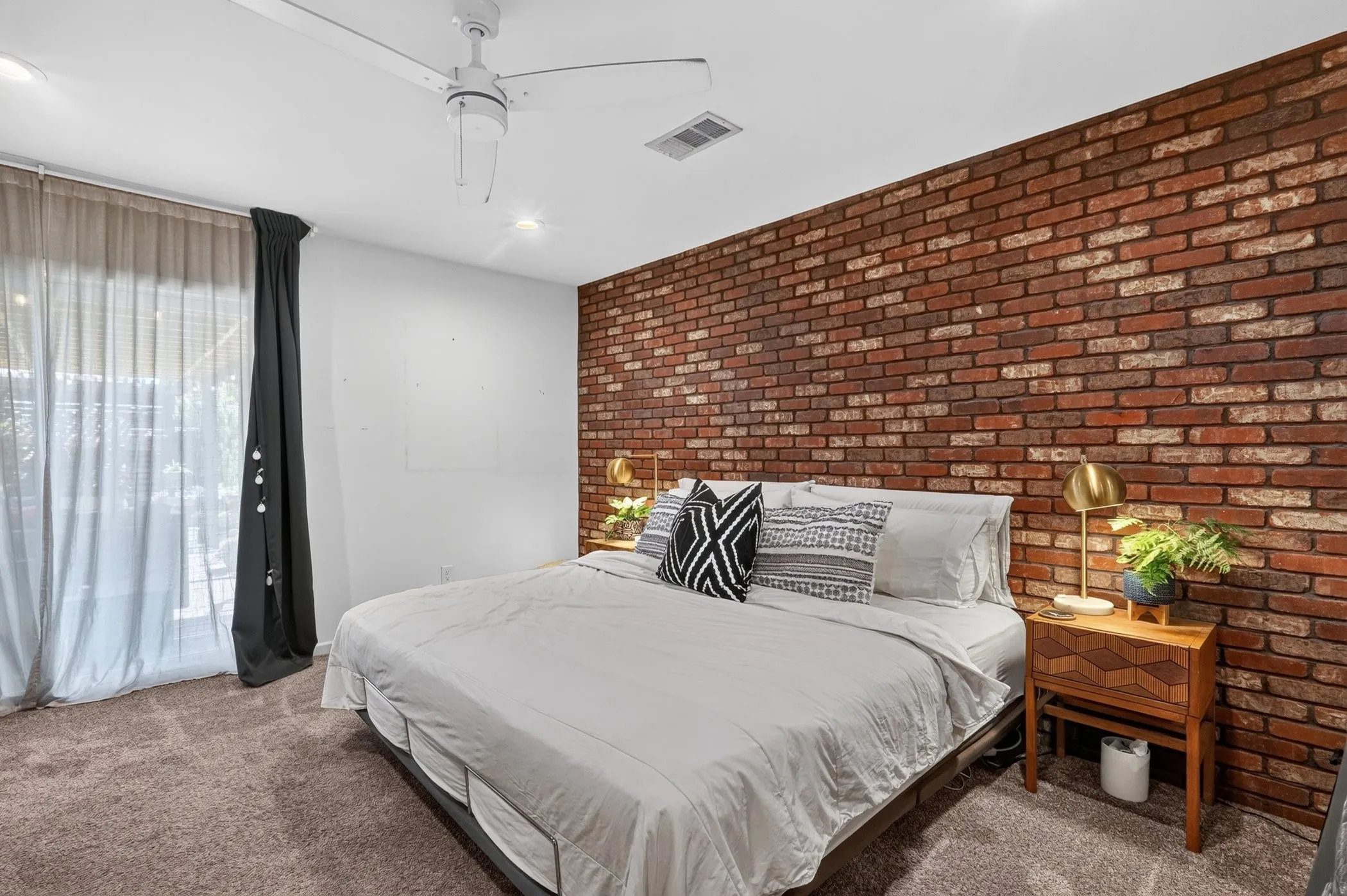 Exposed brick accent wall, recessed lighting, ceiling fan, carpet flooring, and a sliding glass door