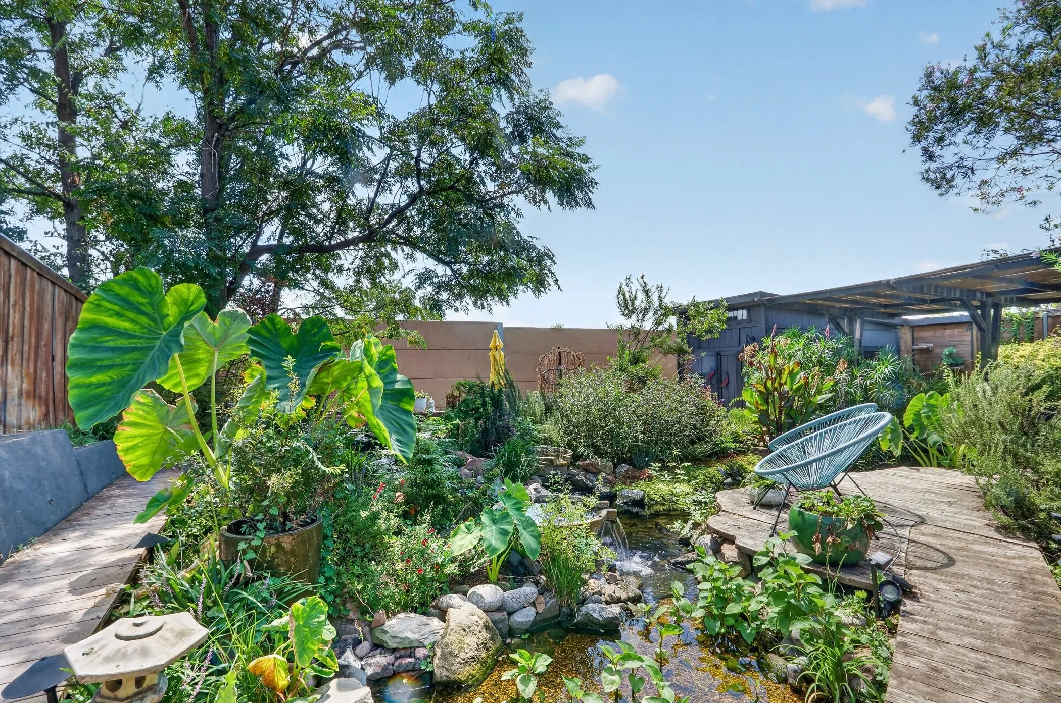 Wood-finish boardwalk, mature trees, dense landscaping, established rock-lined pond