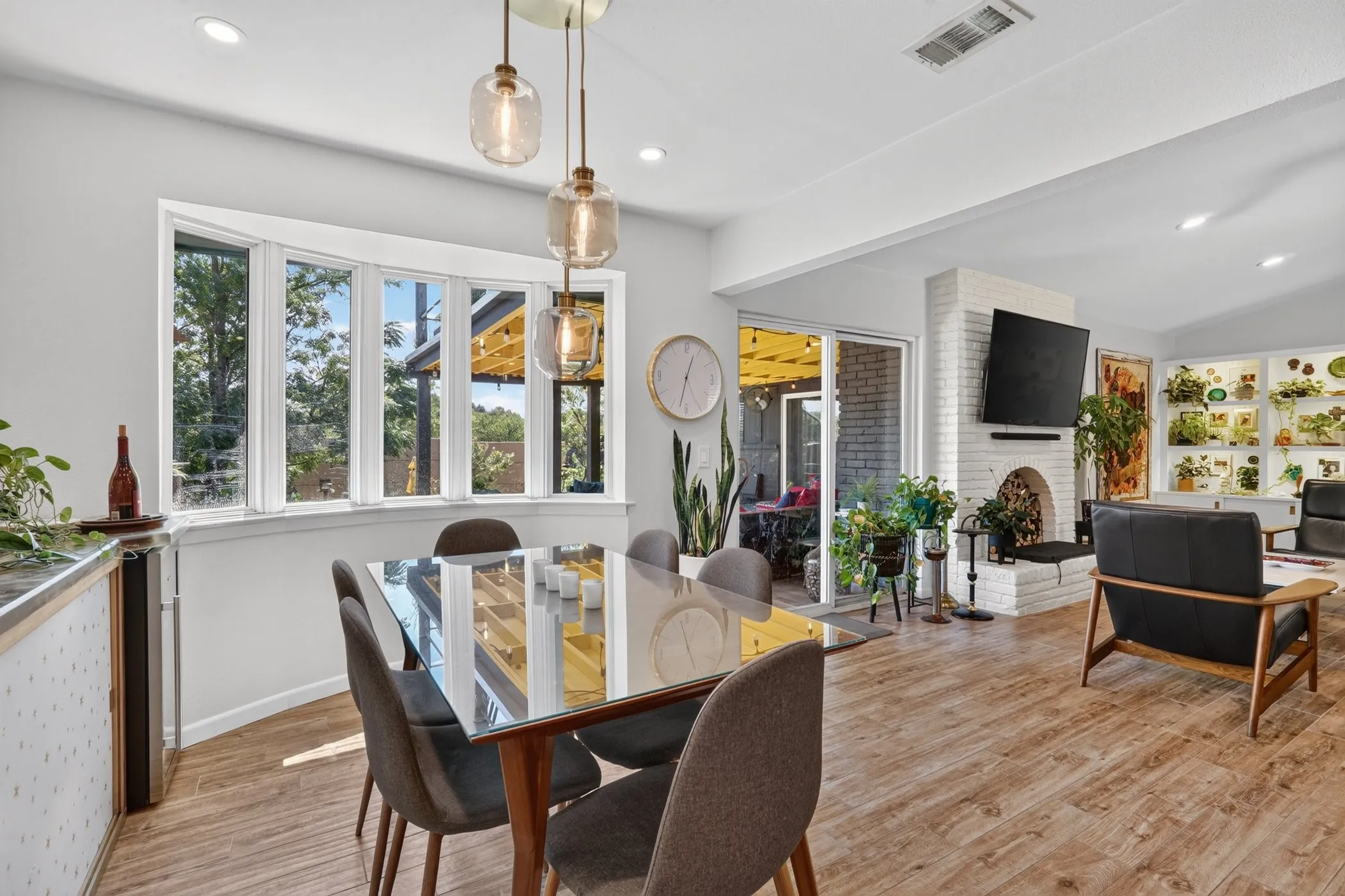 Wood-finish flooring throughout, bay windows, white brick fireplace, sliding glass door, and recessed lighting