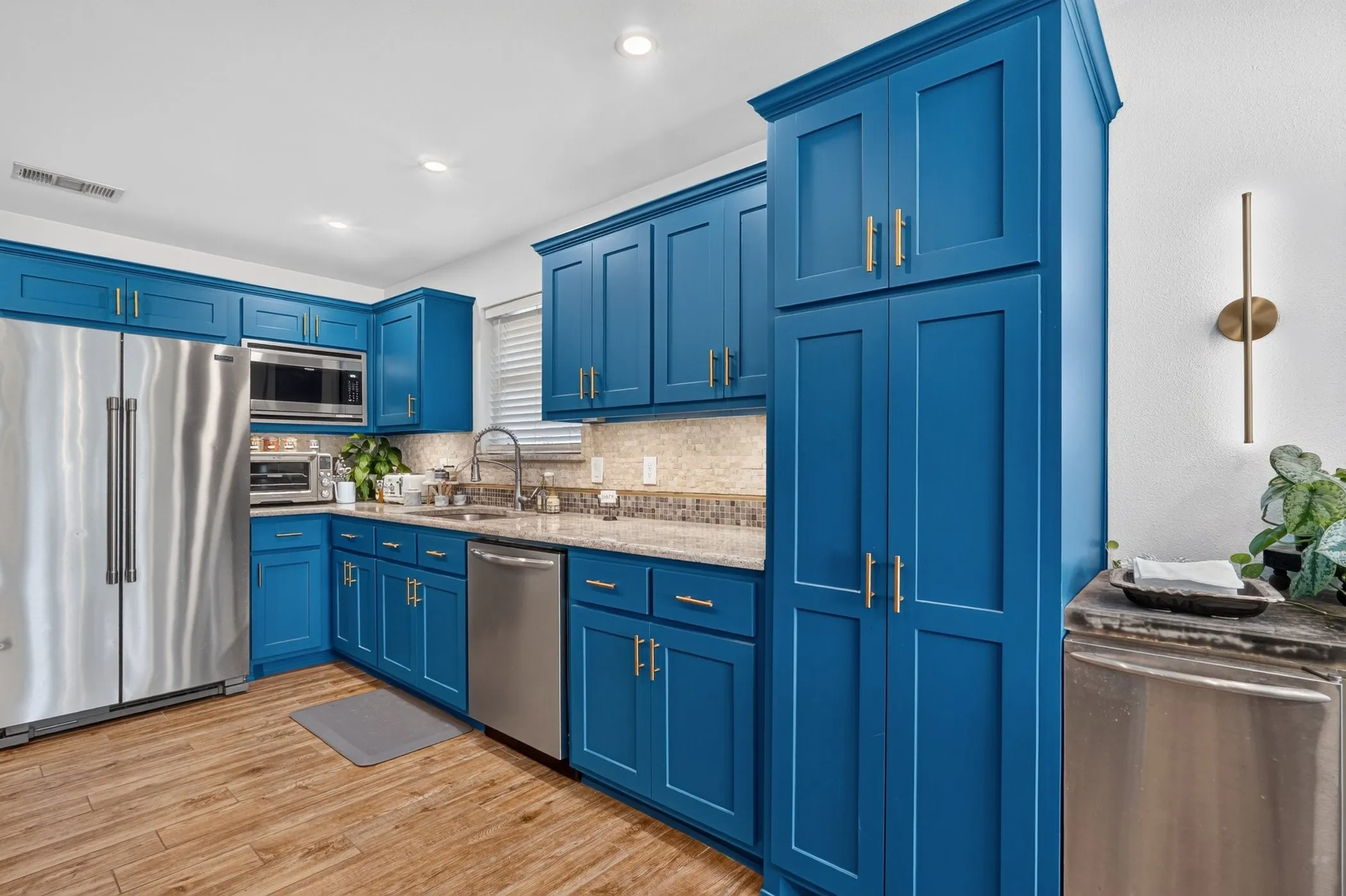 Kitchen featuring blue shaker-style cabinetry, stainless steel appliances, granite-style countertops, mosaic tile backsplash, and wood-finish flooring