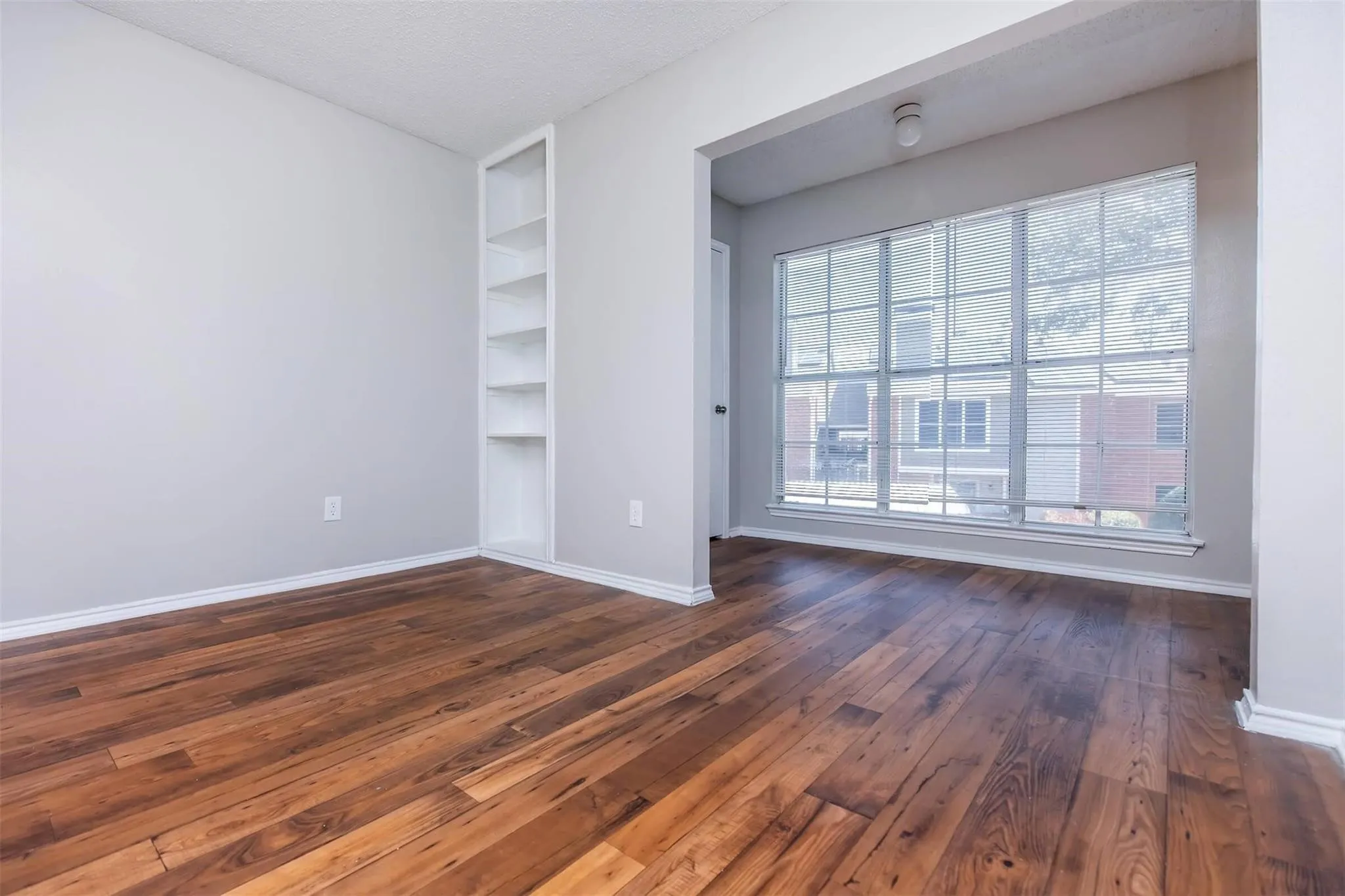 Wood-finish flooring, built-in shelving, white trim, and a large window with horizontal blinds