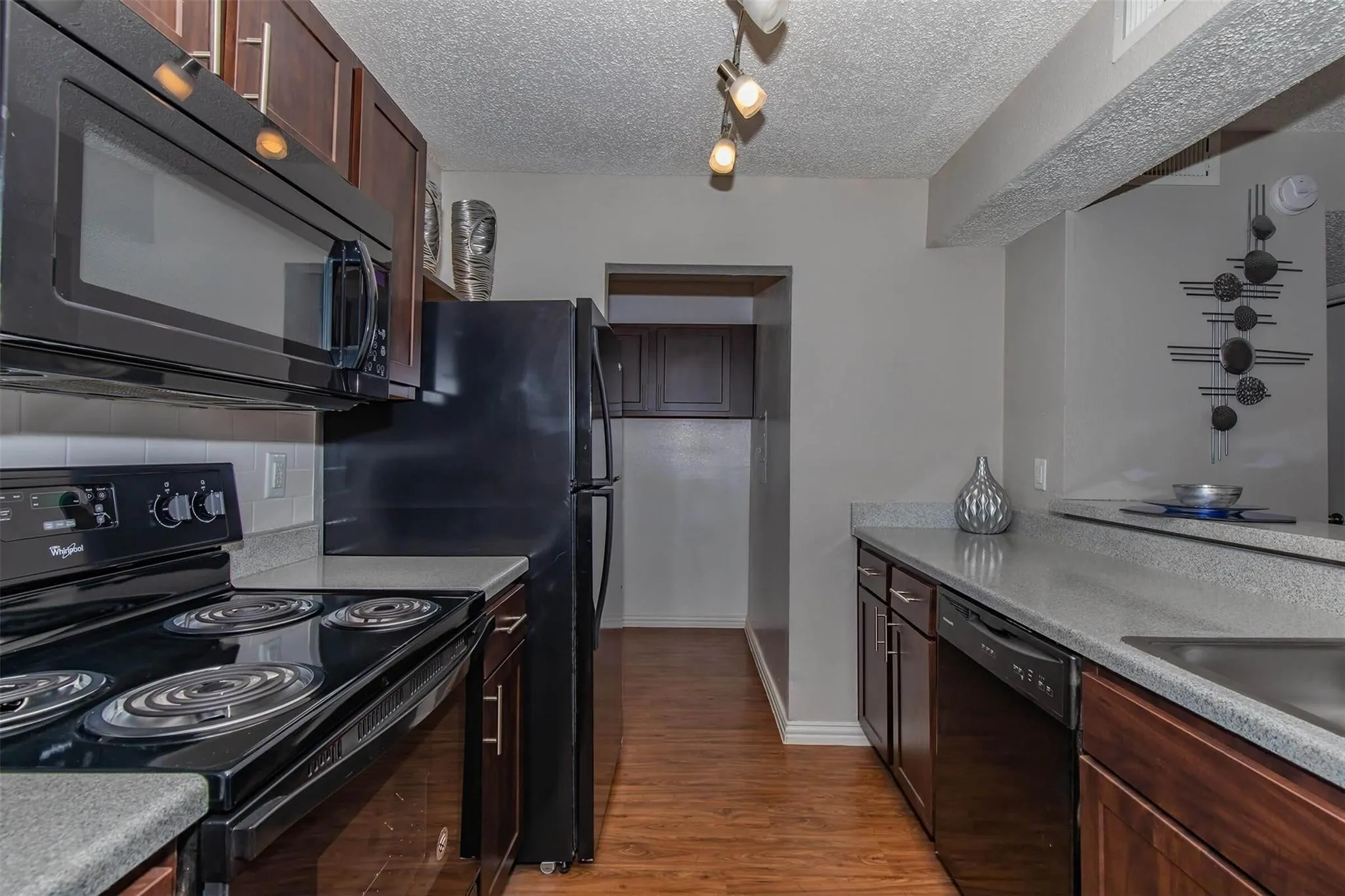 Kitchen featuring wood-finish flooring, dark wood cabinetry, light-toned countertops, and black appliances