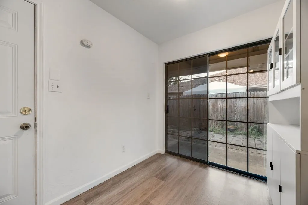 Wood-finish flooring, white paneled door, black-framed sliding glass door, white built-in cabinetry with glass inserts, and black hardware