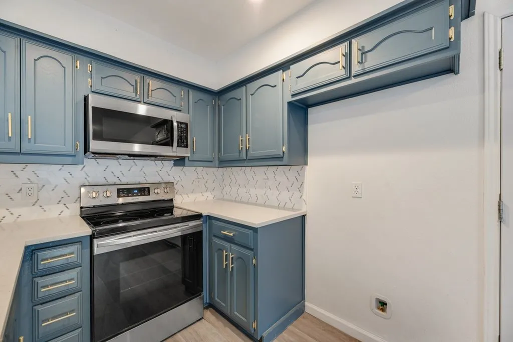 Kitchen featuring blue cabinetry, light countertops, stainless steel appliances, and a patterned tile backsplash