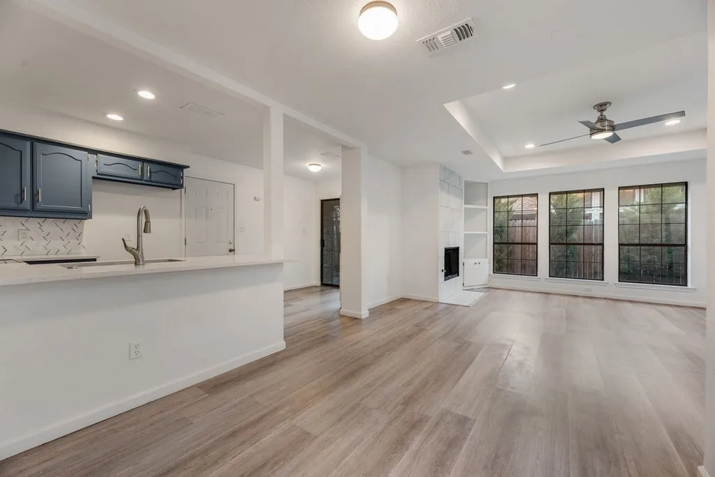 Wood-finish flooring throughout, modern ceiling fan, recessed lighting, accent wall with built-in shelving and fireplace, and three large windows