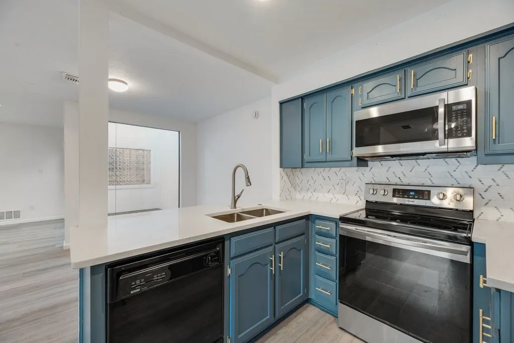 Kitchen featuring blue cabinetry, a stainless steel sink, a stainless steel microwave, a stainless steel range, and a white countertop