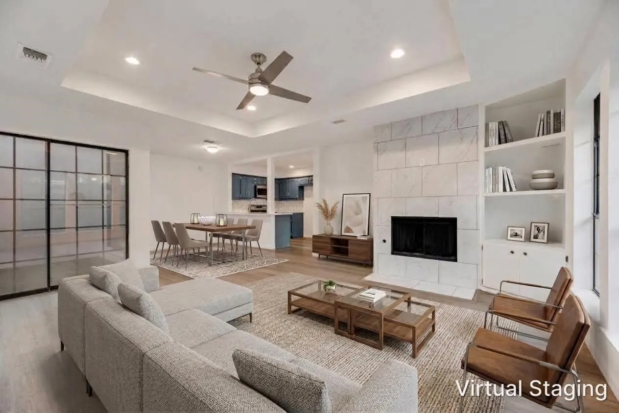 Spacious living area featuring wood-finish flooring, a tray ceiling with recessed lighting, a fireplace with a stone surround, and built-in shelving