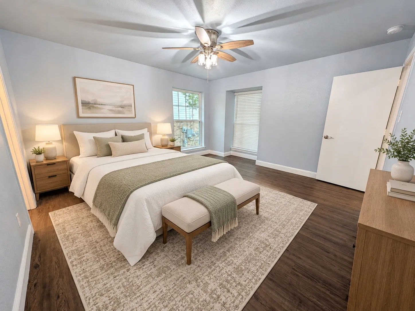Wood-finish flooring with light blue walls, two windows with blinds, and a ceiling fan with light fixture