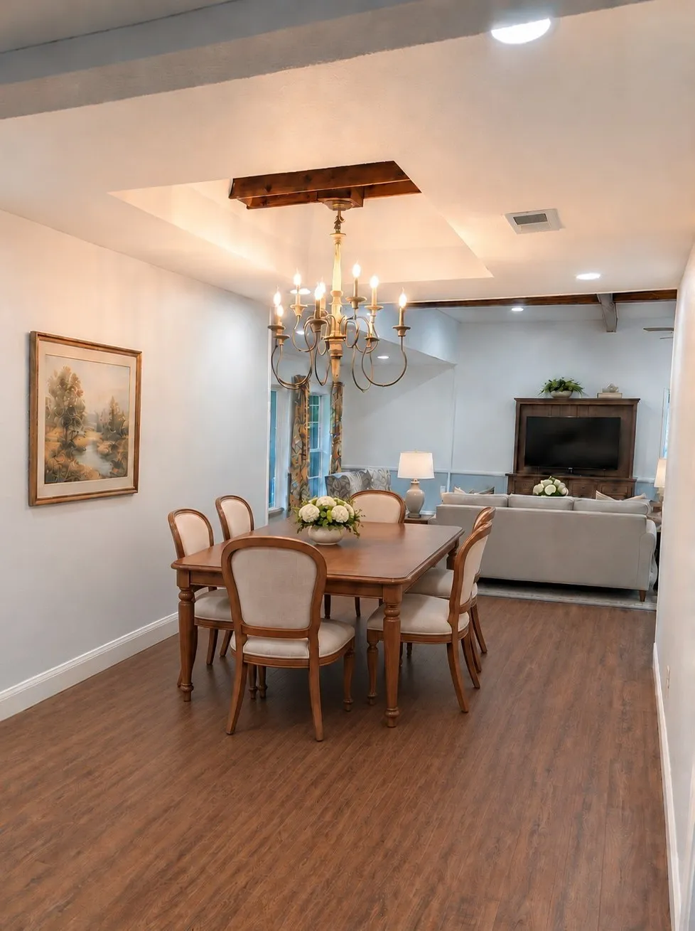 Recessed ceiling with a chandelier, wood-finish flooring, and white walls