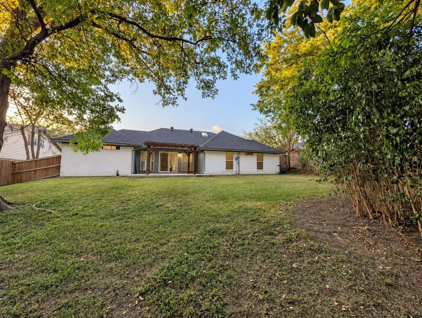 Expansive backyard with a manicured lawn, complete with a pergola over the patio, and a privacy fence
