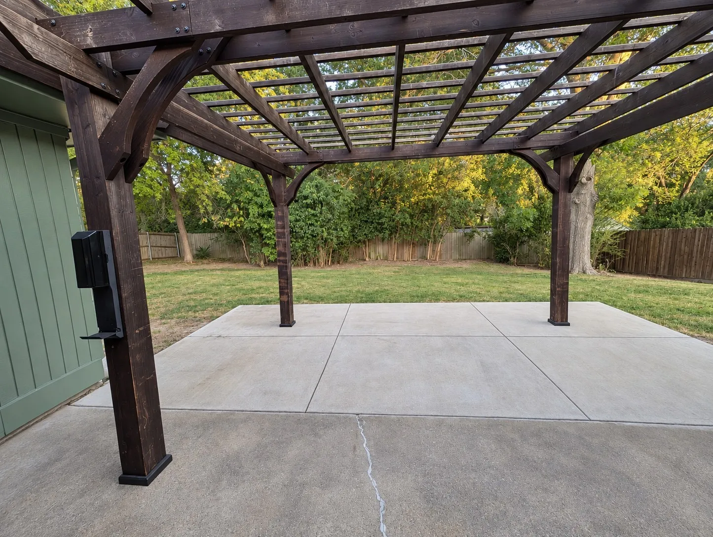 Expansive concrete patio with a dark wood pergola, providing an outdoor entertaining space