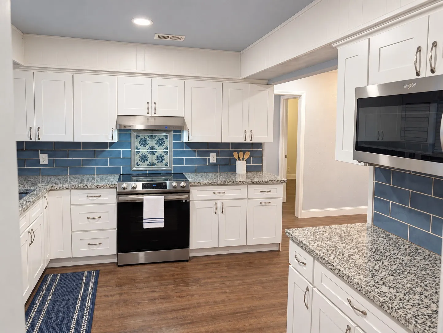 White shaker cabinetry with granite countertops, stainless steel appliances, blue subway tile backsplash, and wood-finish flooring