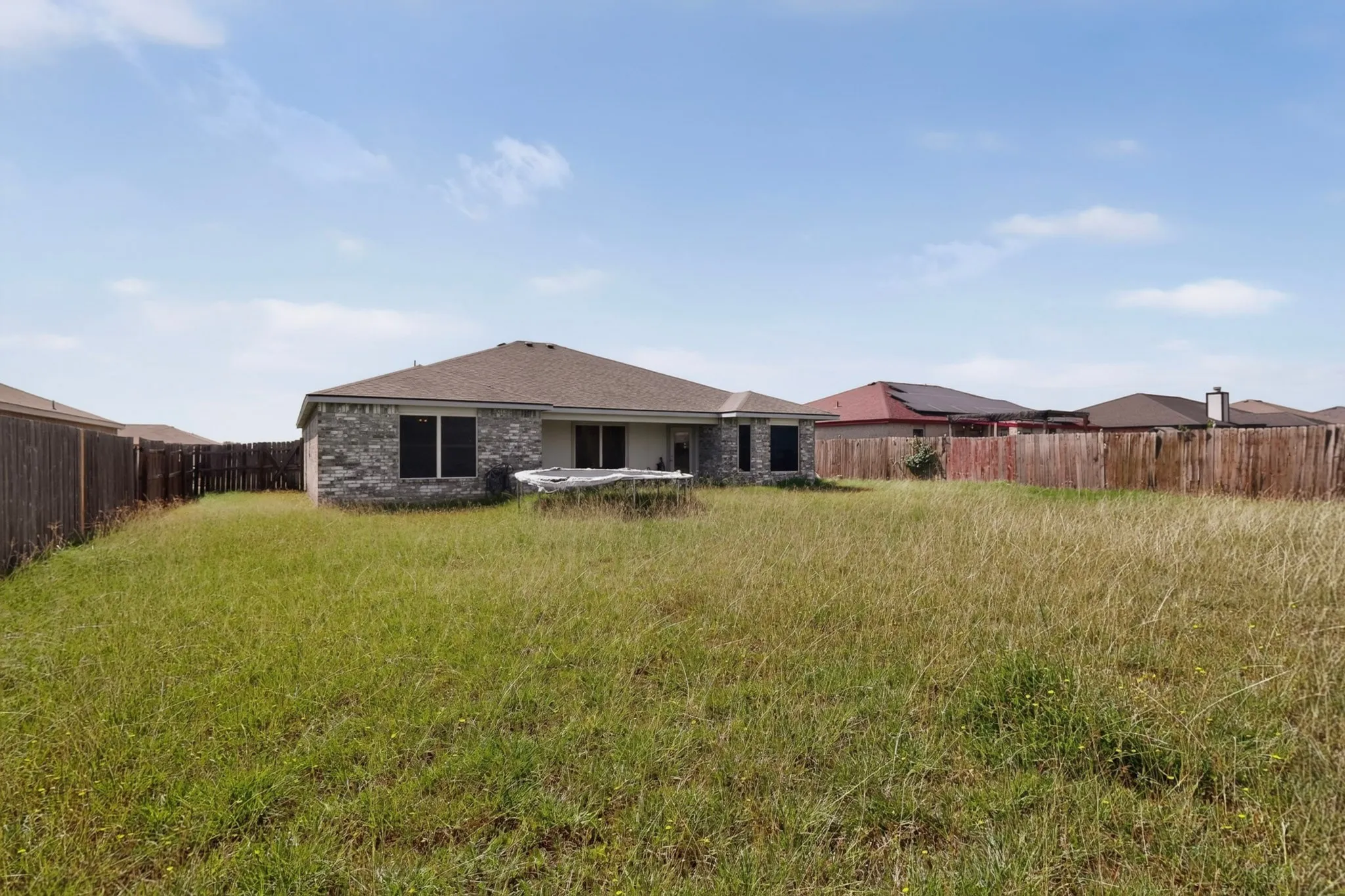 Expansive backyard space with perimeter fencing, a stone exterior, and a composition shingle roof