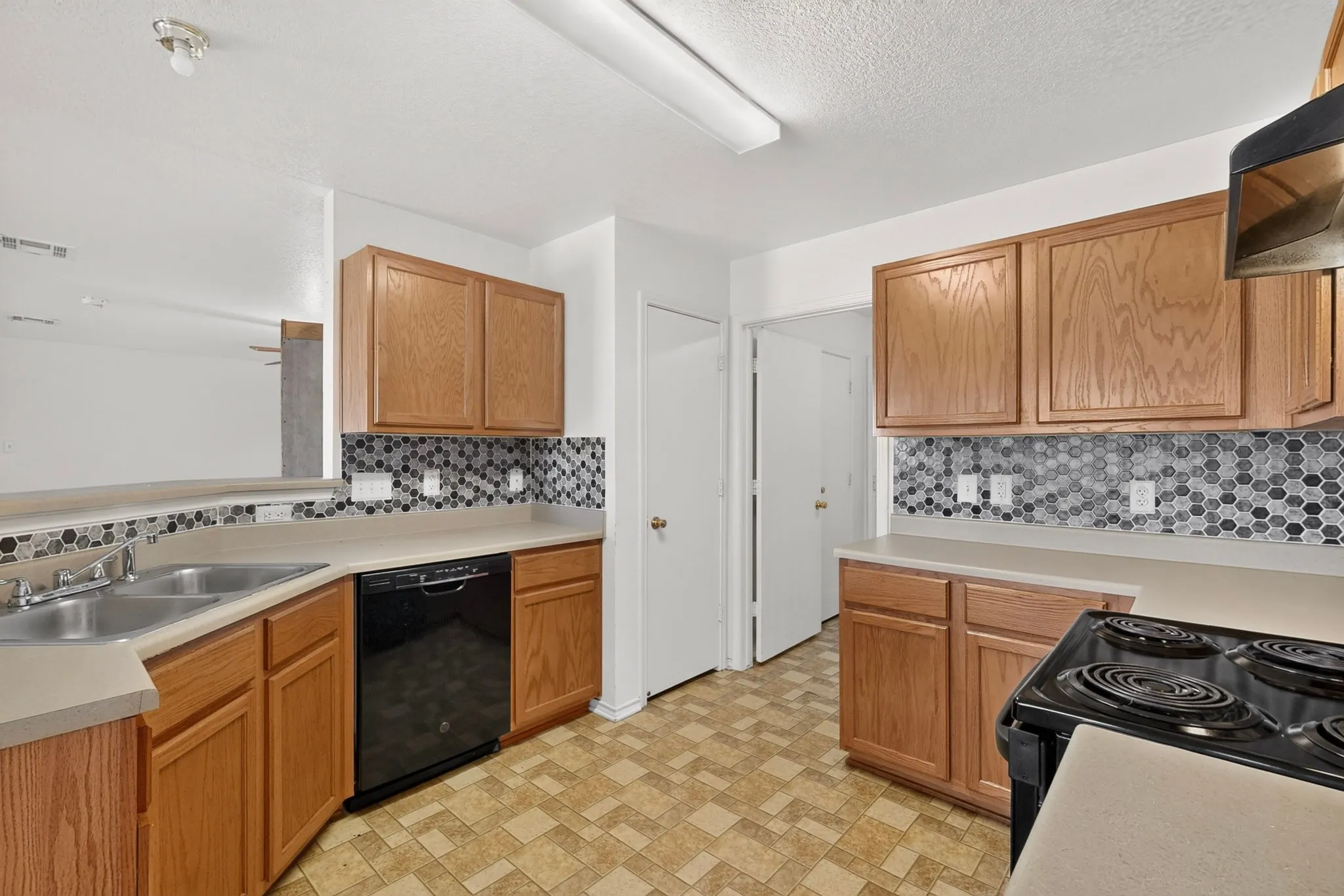 Kitchen with wood cabinetry, a mosaic tile backsplash, dual basin stainless steel sink, and a black built-in dishwasher