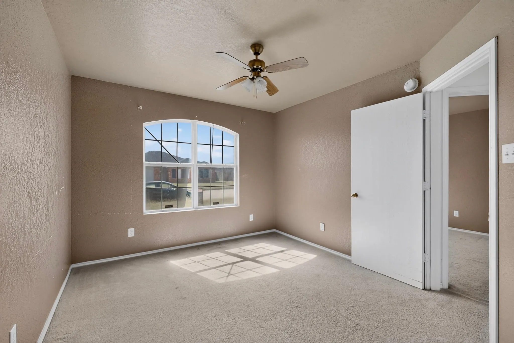 Arched window with gridded panes, ceiling fan, and neutral carpet flooring