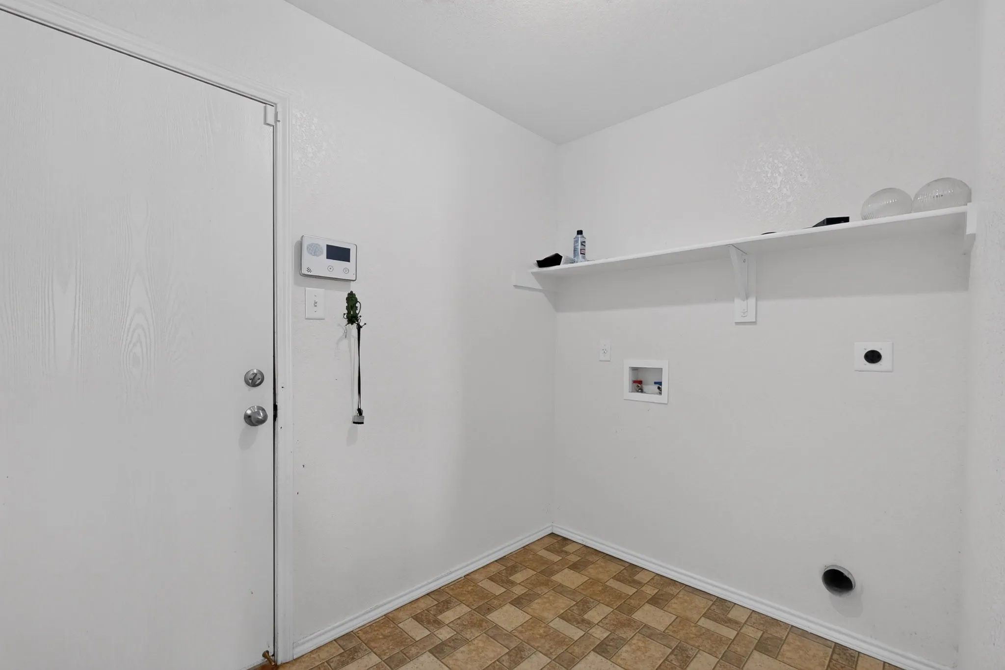 Utility room featuring patterned floor tile, white walls, and a wall-mounted shelf
