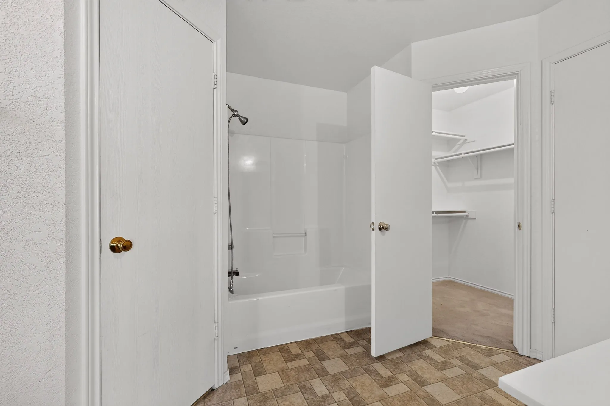 White bathtub and shower combination, with a built-in shelf, adjacent to a walk-in closet featuring multiple shelving units