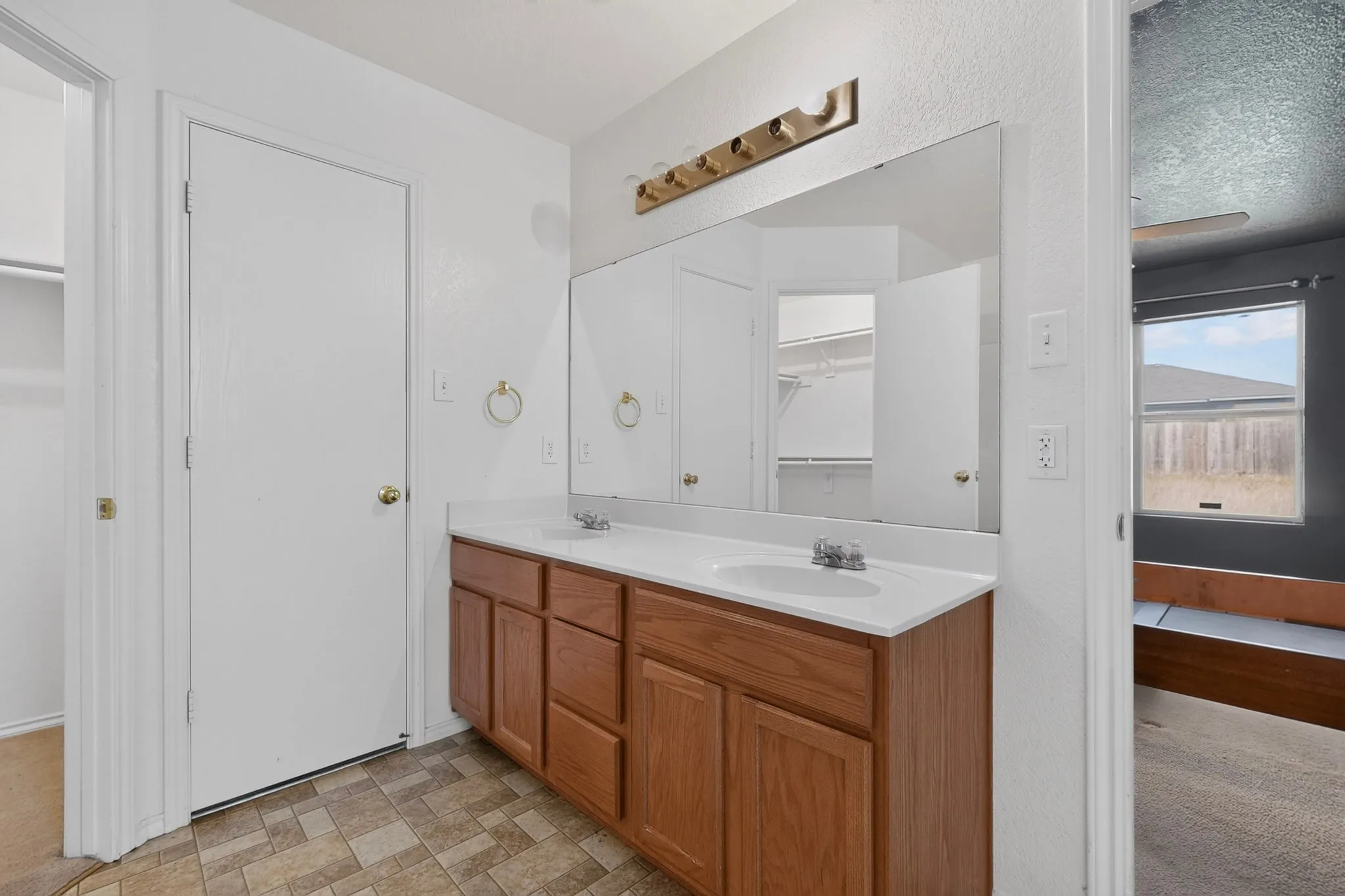 Dual vanity with integrated sinks, wood-finish cabinetry, and a large wall-mounted mirror
