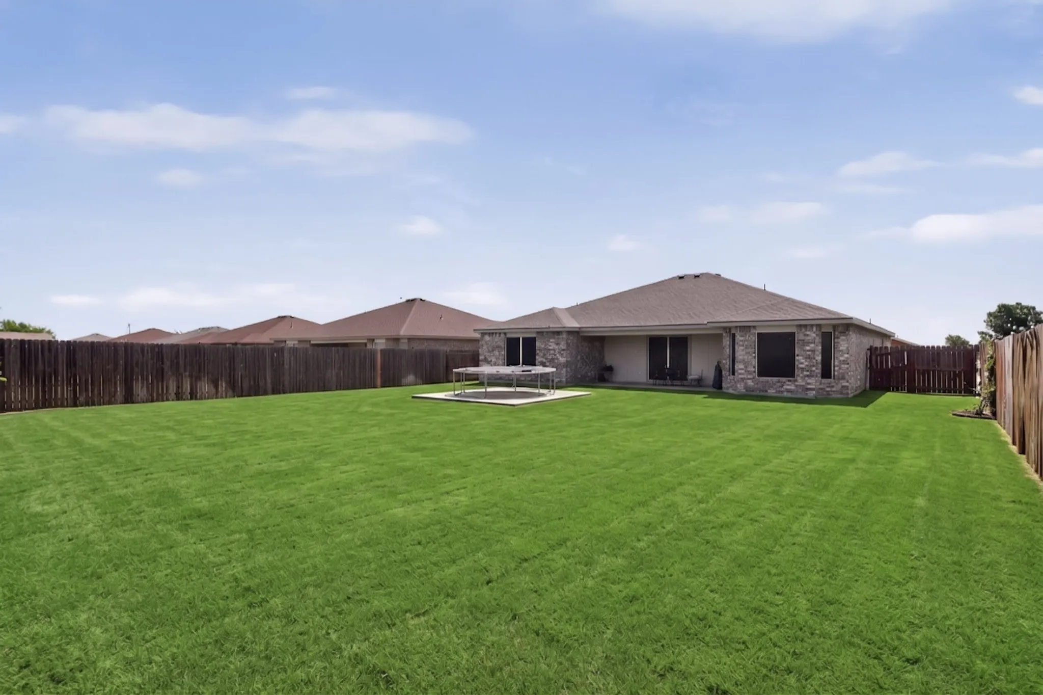 Expansive backyard featuring a manicured lawn, a full privacy fence, and a stone-accented exterior