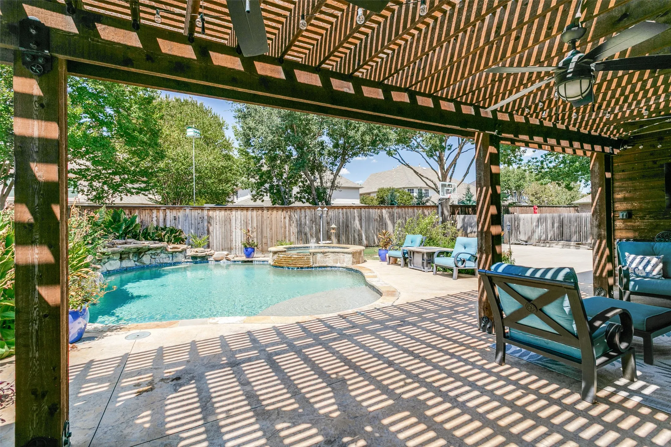 Expansive outdoor living area featuring a pergola, ceiling fans, a swimming pool with a water feature, and a privacy fence