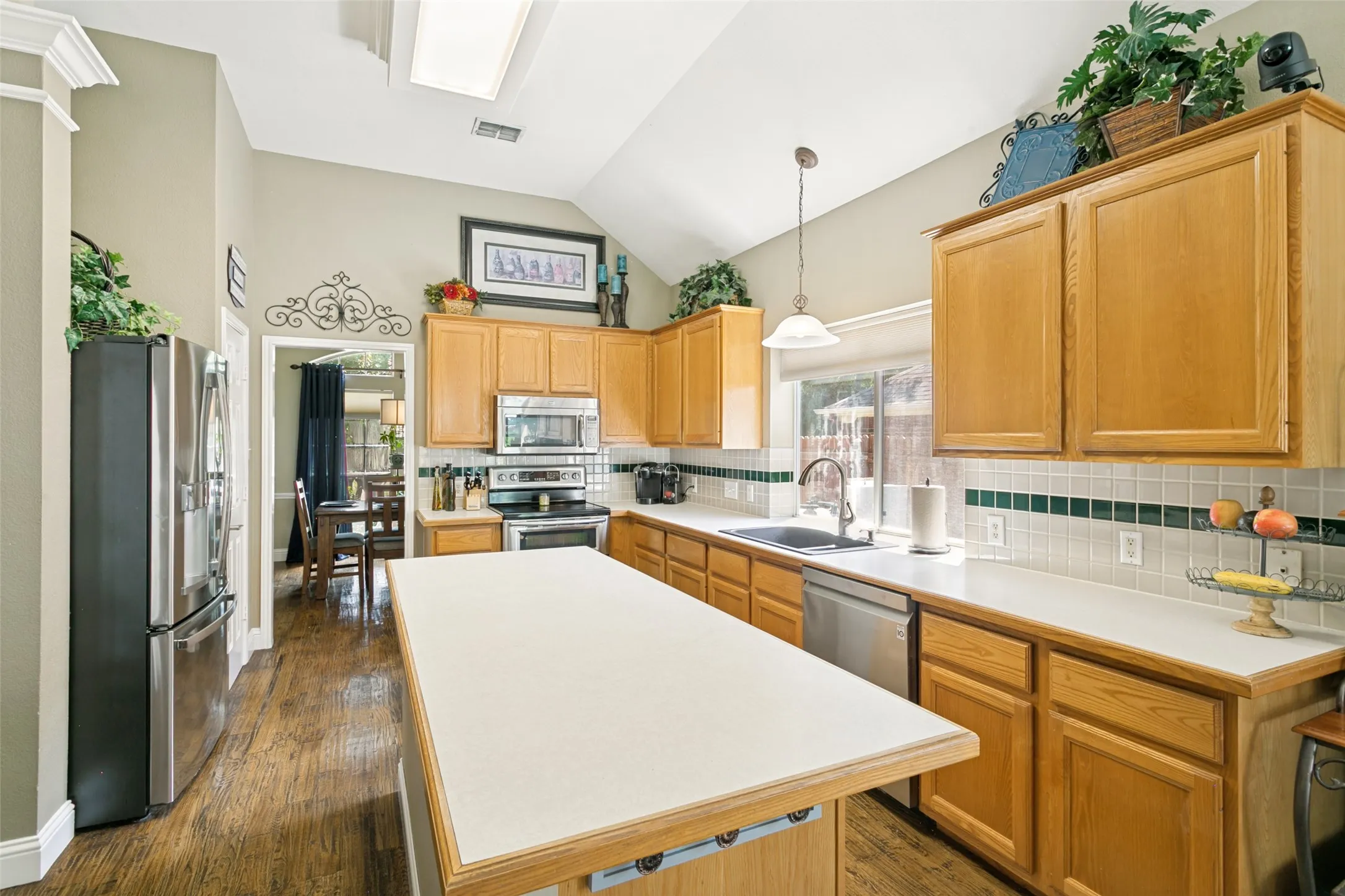 Kitchen featuring wood-finish cabinetry, stainless steel appliances, a center island with a light-toned countertop, and a vaulted ceiling with a skylight