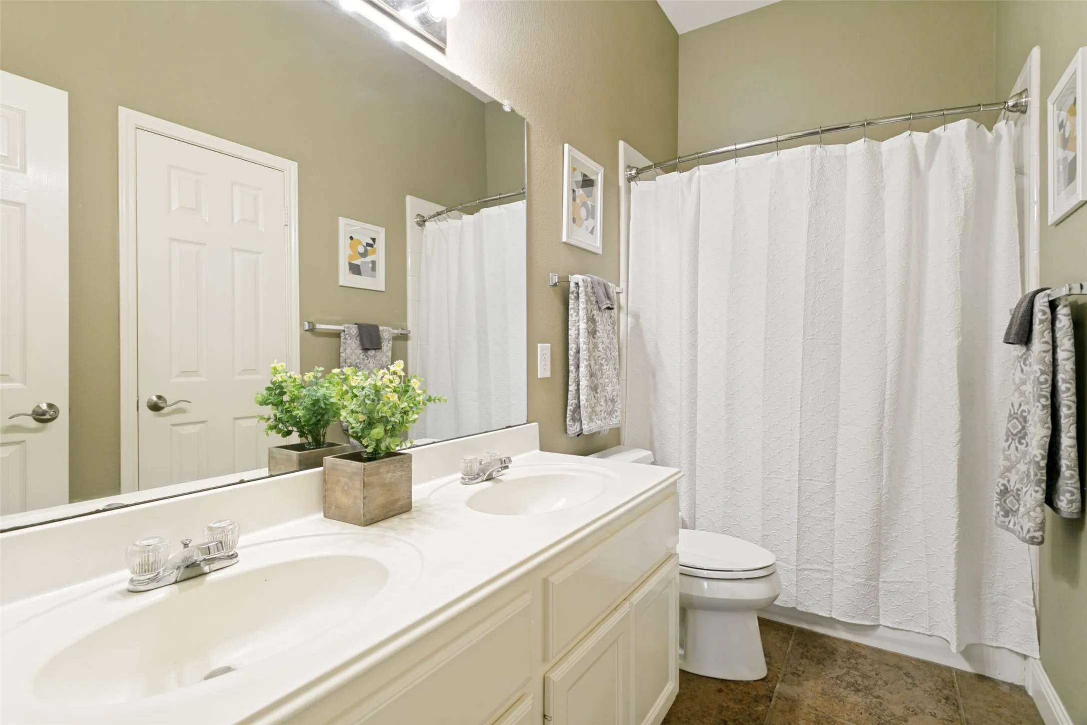 Bathroom featuring a dual-sink vanity with ample counter space, a large wall-mounted mirror, and a shower/tub combination with a white shower curtain