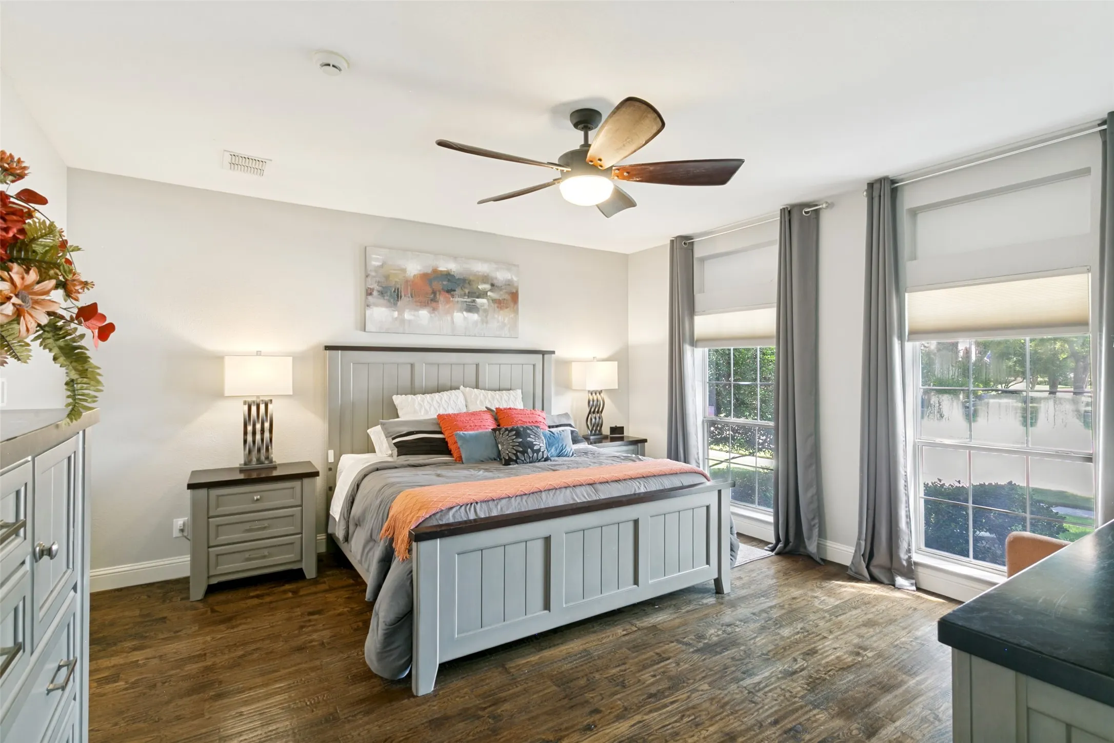 Primary bedroom with Hardwood-finish flooring, ceiling fan with integrated lighting, multiple windows with roller shades