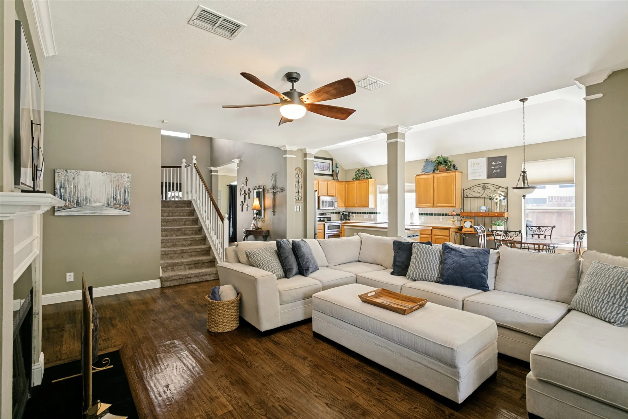 Open-concept living area featuring wood-finish flooring, a ceiling fan, and a fireplace with a white mantle