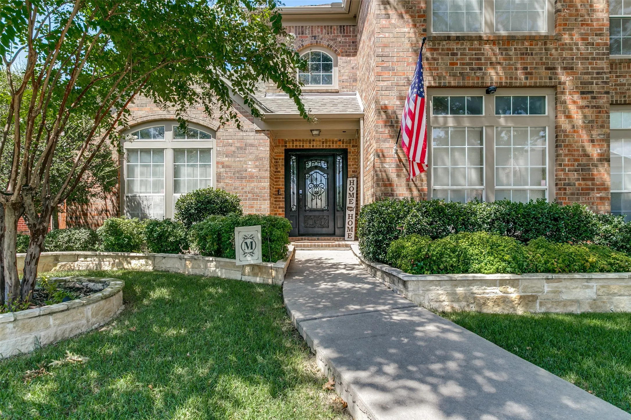 Brick facade with arched windows, an intricate front door, and established landscaping