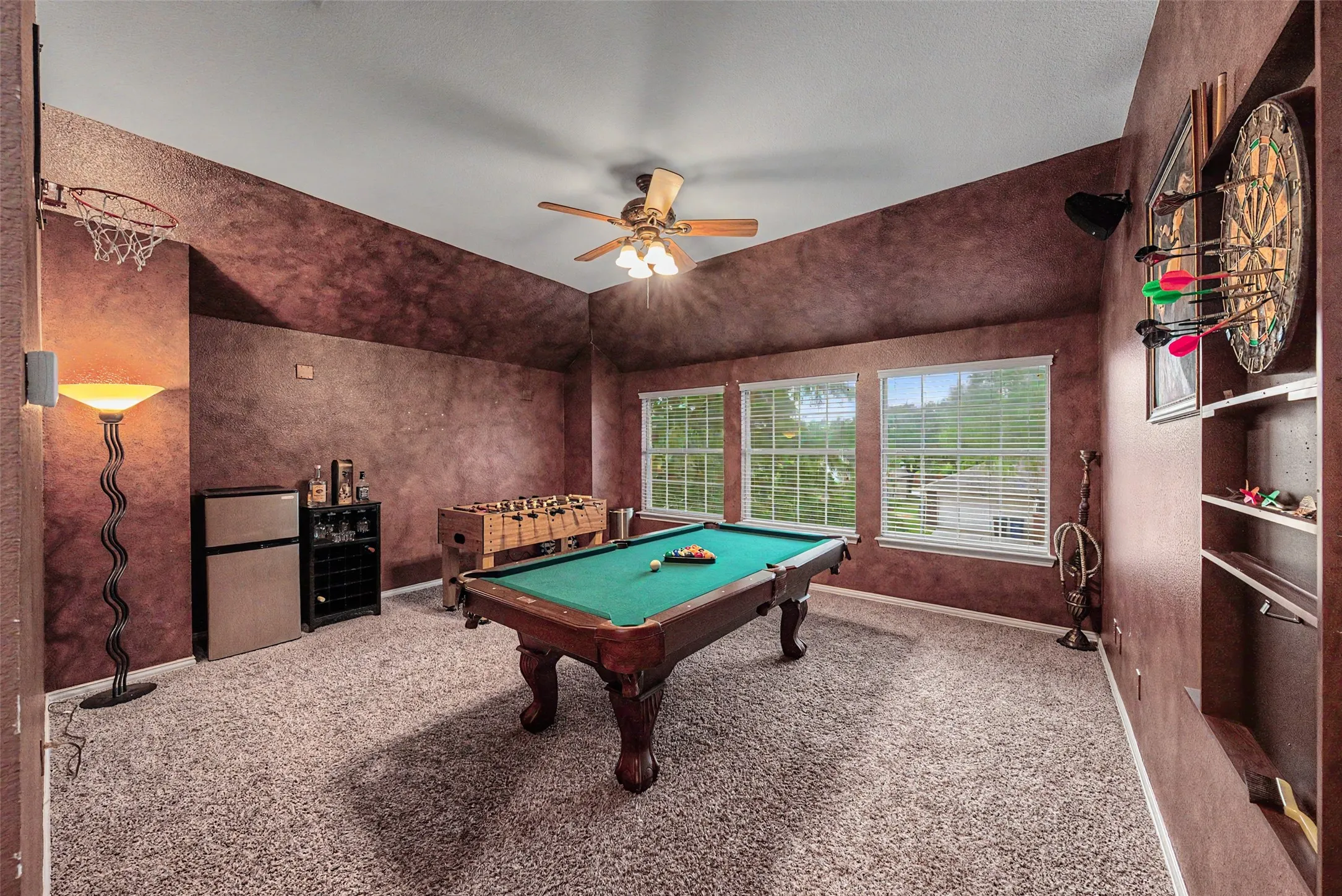 Carpeted recreation room featuring a ceiling fan, three windows, and built-in shelving