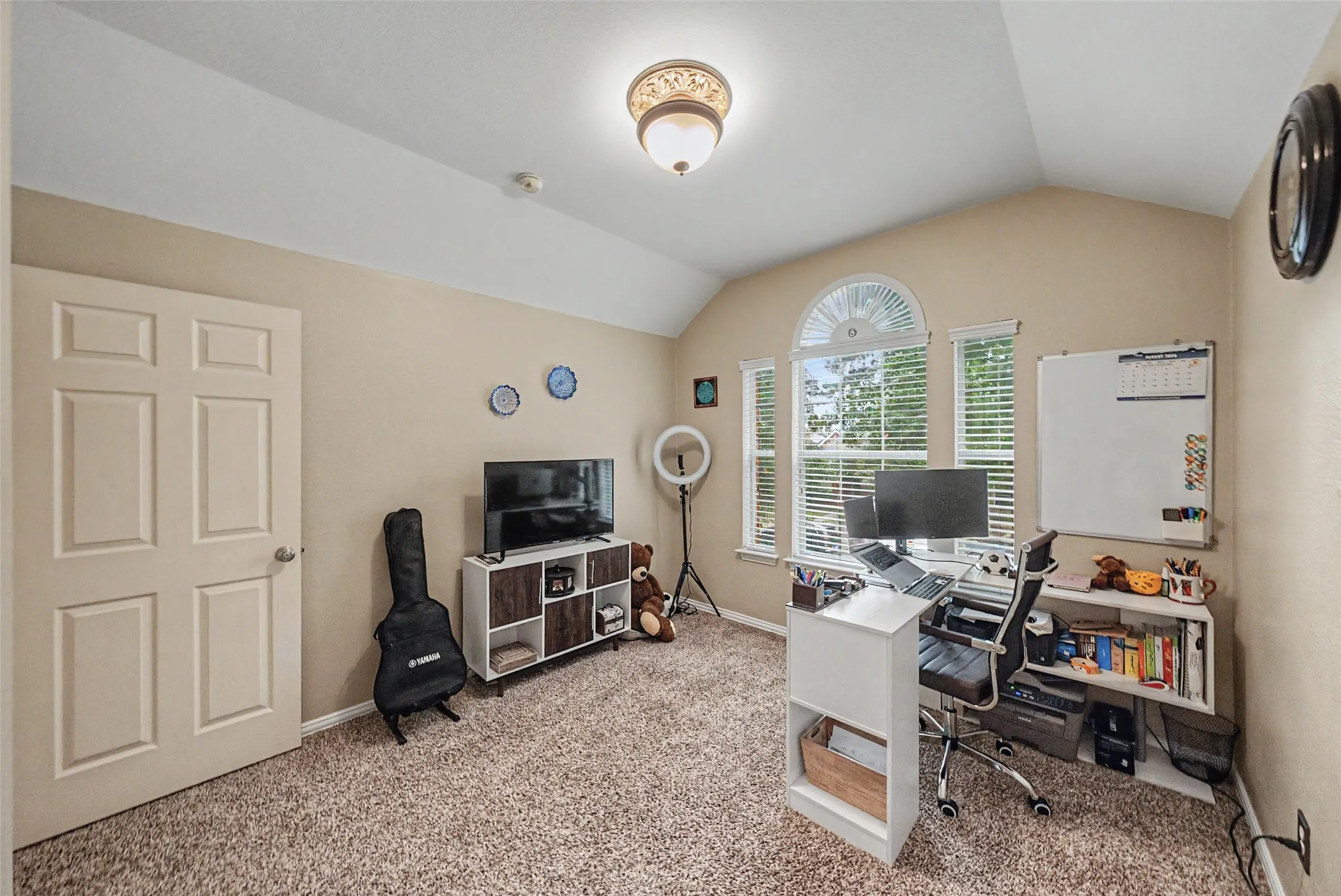 Vaulted ceiling with an ornate flush mount light fixture, carpeted flooring, and a multi-pane arched window