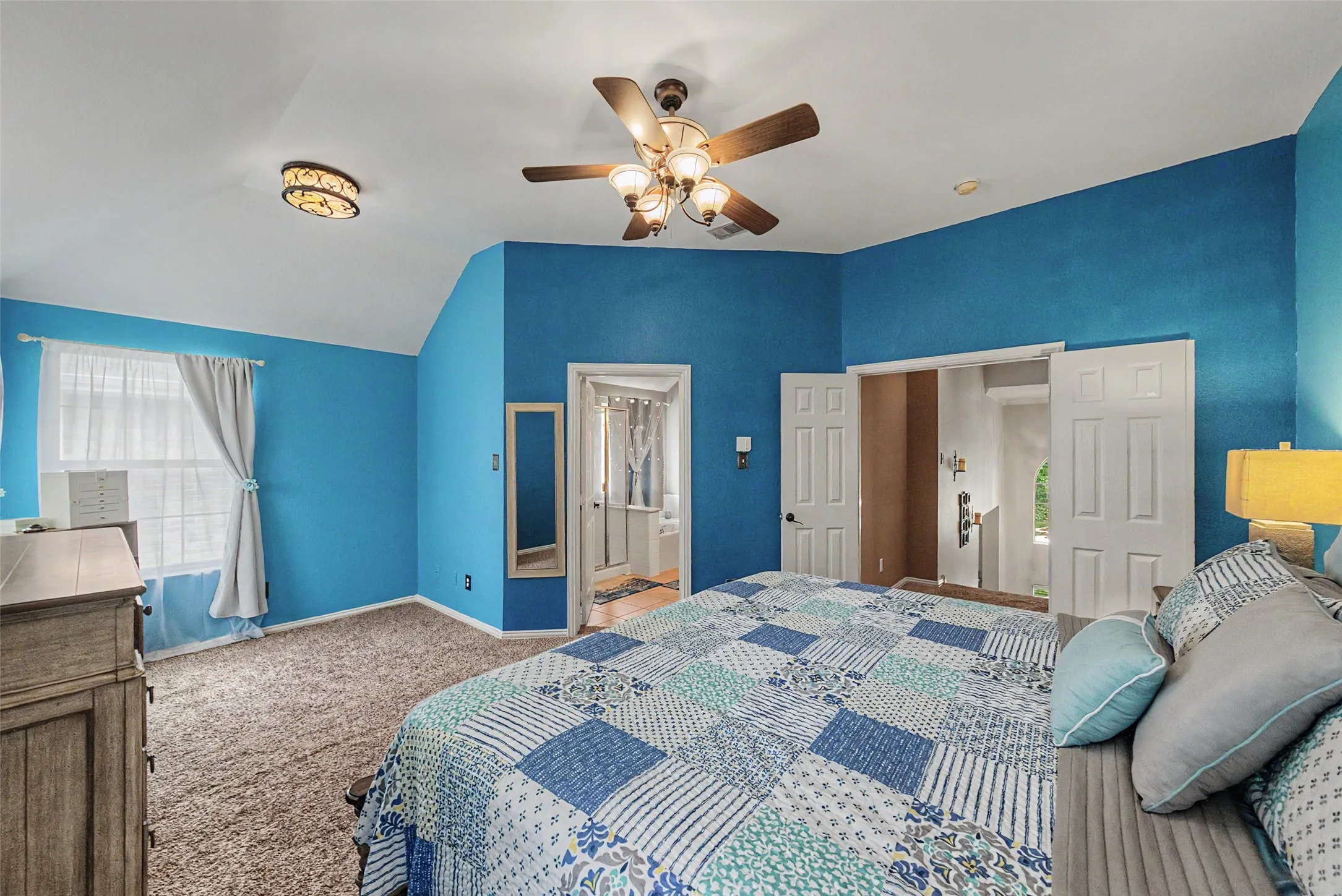 Vaulted ceiling with a ceiling fan, carpeted flooring, and a window with sheer curtains