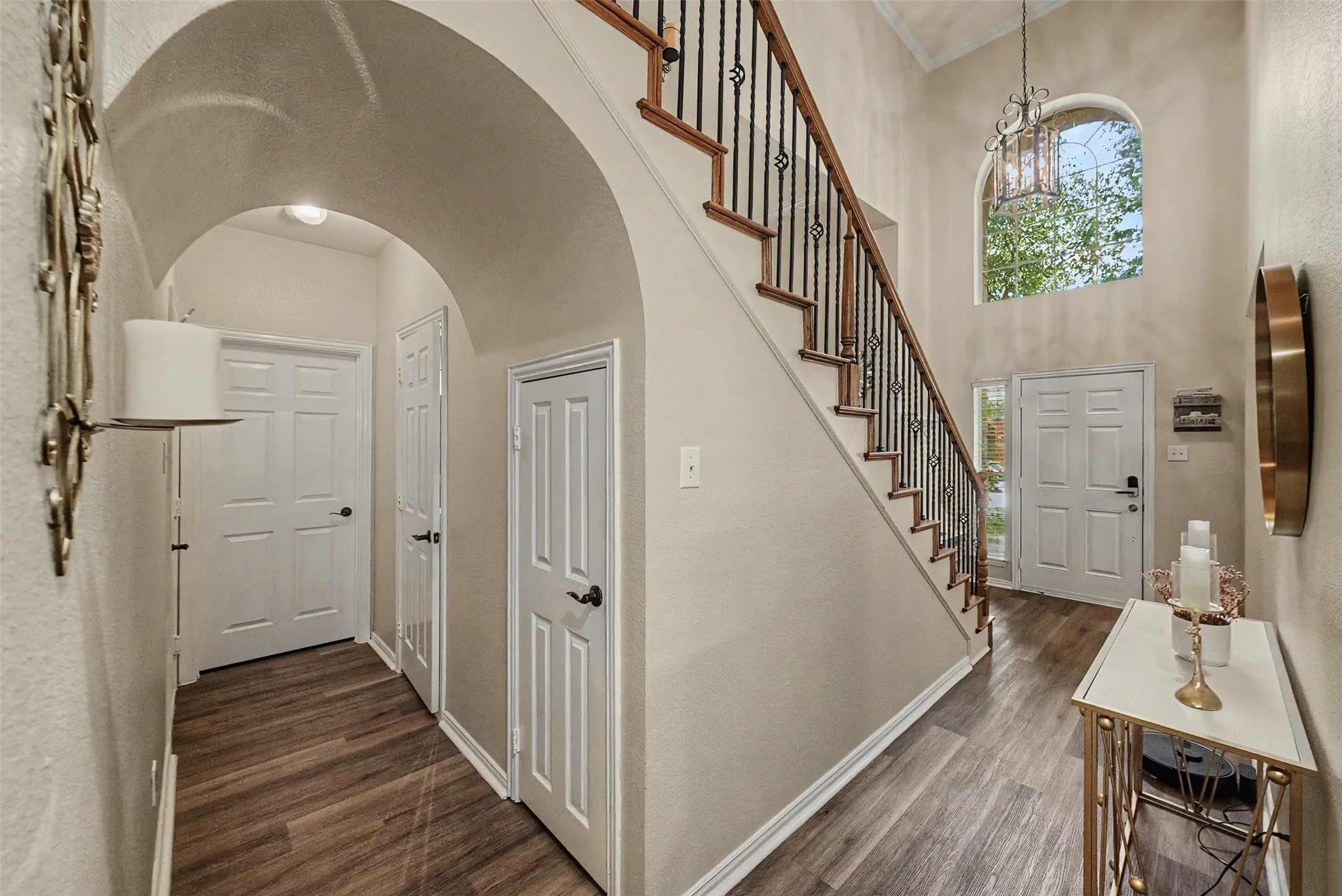 Double-height entryway featuring wood-finish flooring, an arched doorway, and a prominent staircase with wrought iron balusters