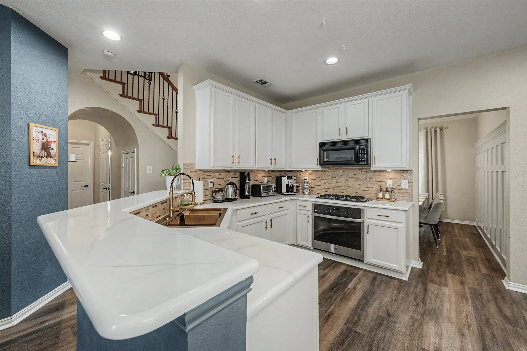 Modern kitchen featuring white cabinetry, light-toned countertops, a stainless steel oven, a copper-finish sink with a brass faucet, and wood-finish flooring