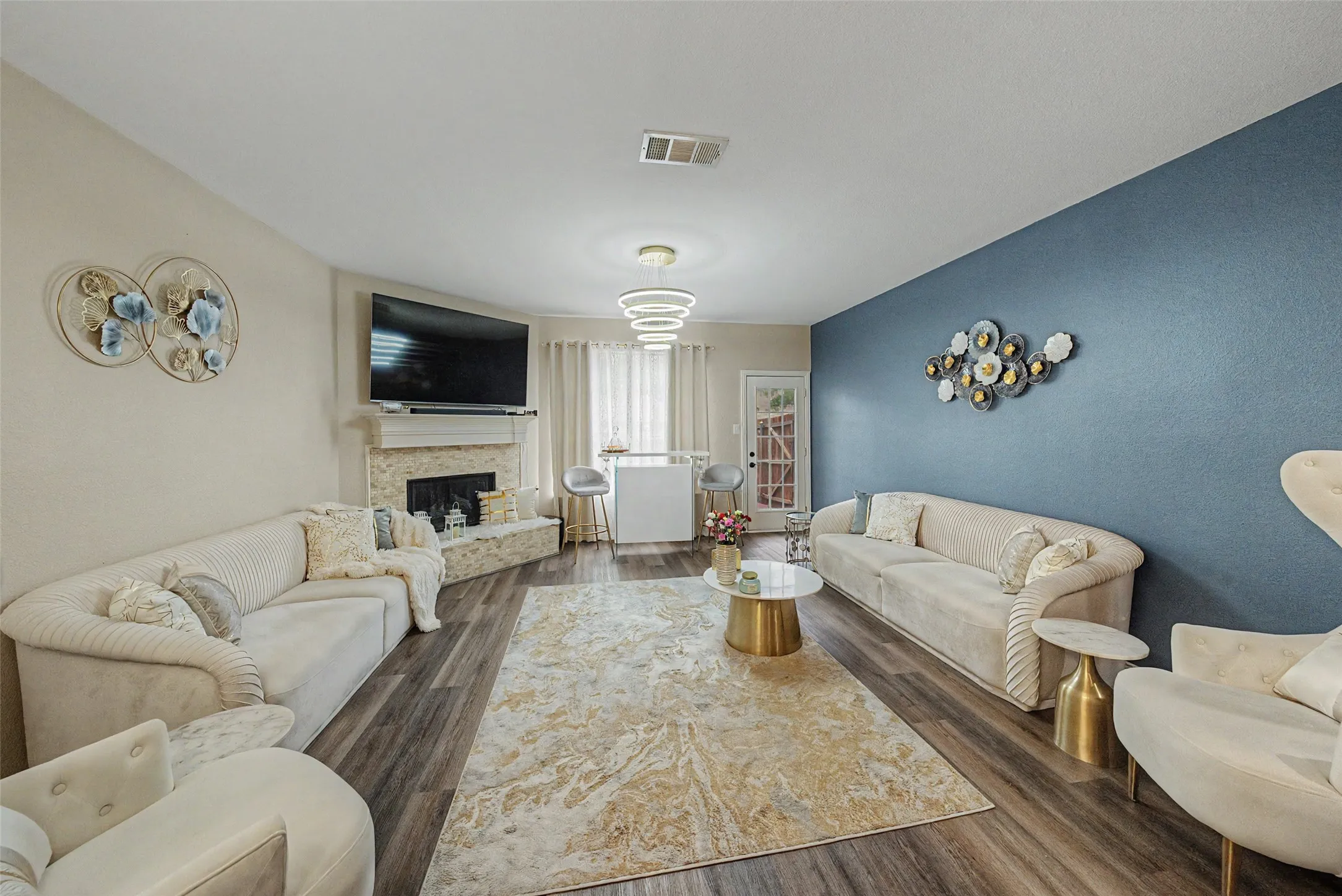 Living area featuring wood-finish flooring, a stone-clad fireplace, and a light fixture with multiple rings