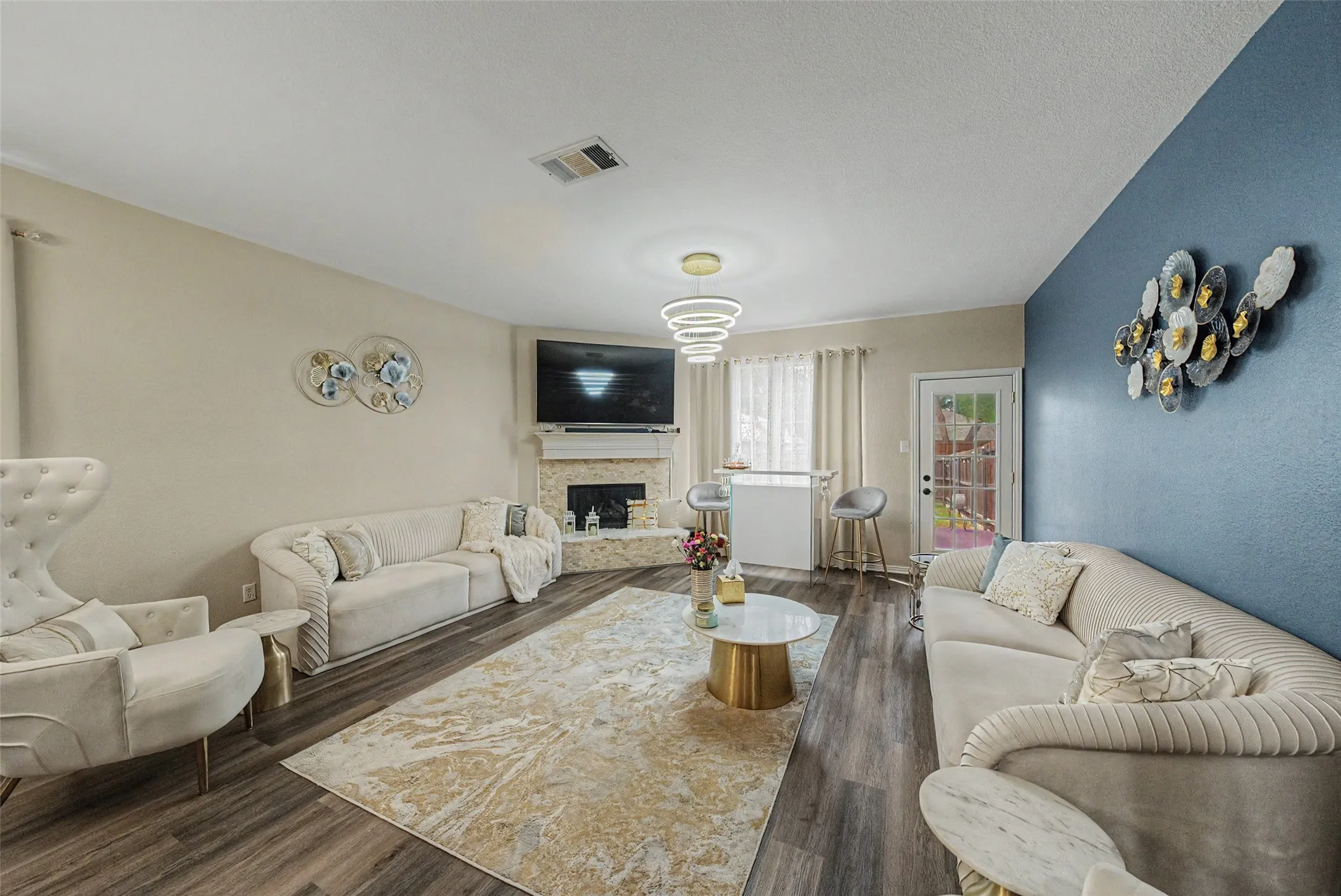 Wood-finish flooring, corner fireplace with stone surround, recessed lighting, modern tiered ceiling light fixture, and a glass-paned door