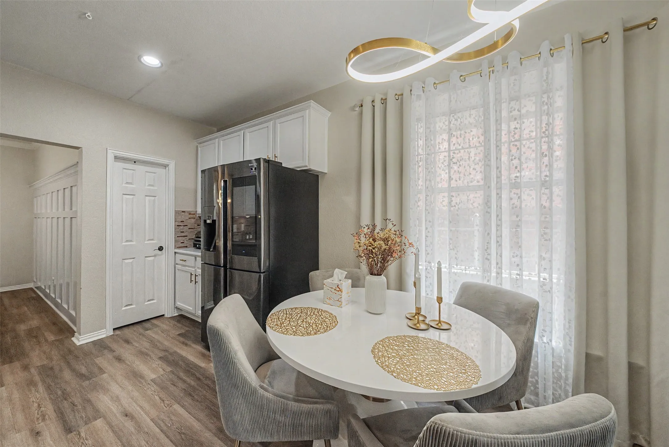 White shaker cabinetry, wood-finish flooring, and a stainless steel refrigerator