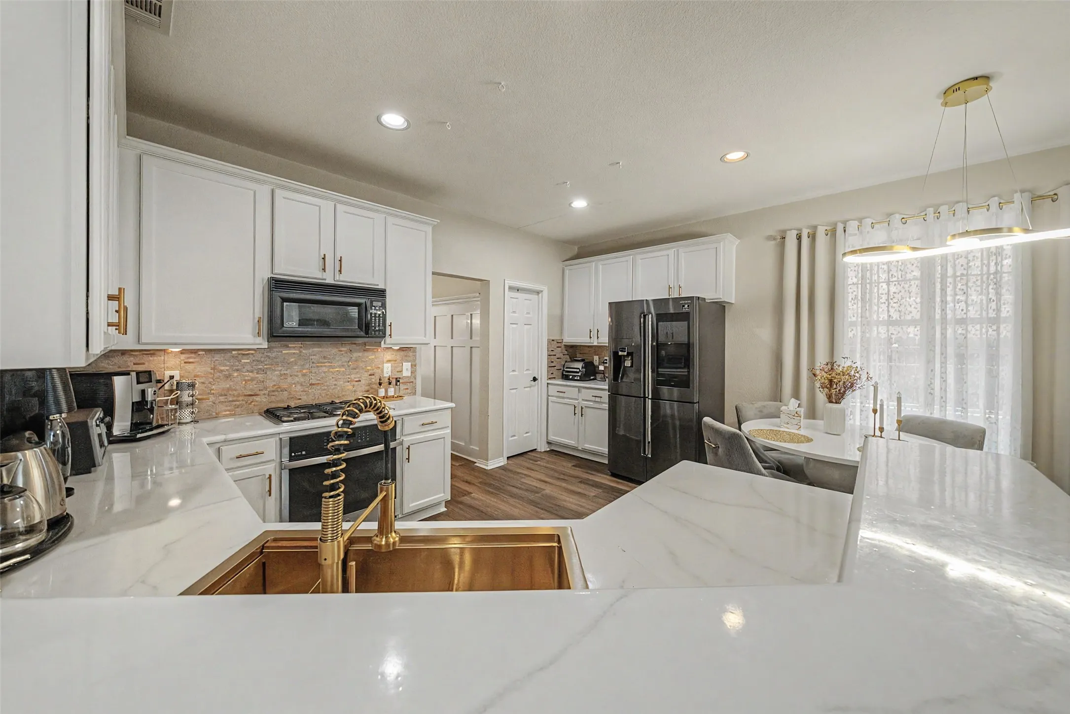 White shaker-style cabinetry with gold-tone hardware, white countertops, wood-finish flooring, and a gold-tone sink with a matching faucet