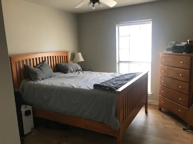 Wood-finish flooring with a neutral wall color, a ceiling fan with light fixture, and a window featuring blinds