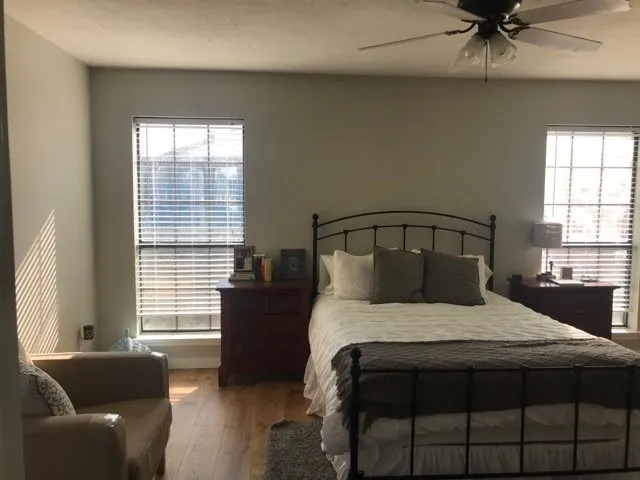 Room featuring wood-finish flooring, two windows with blinds, a ceiling fan with integrated lighting, and neutral wall tones