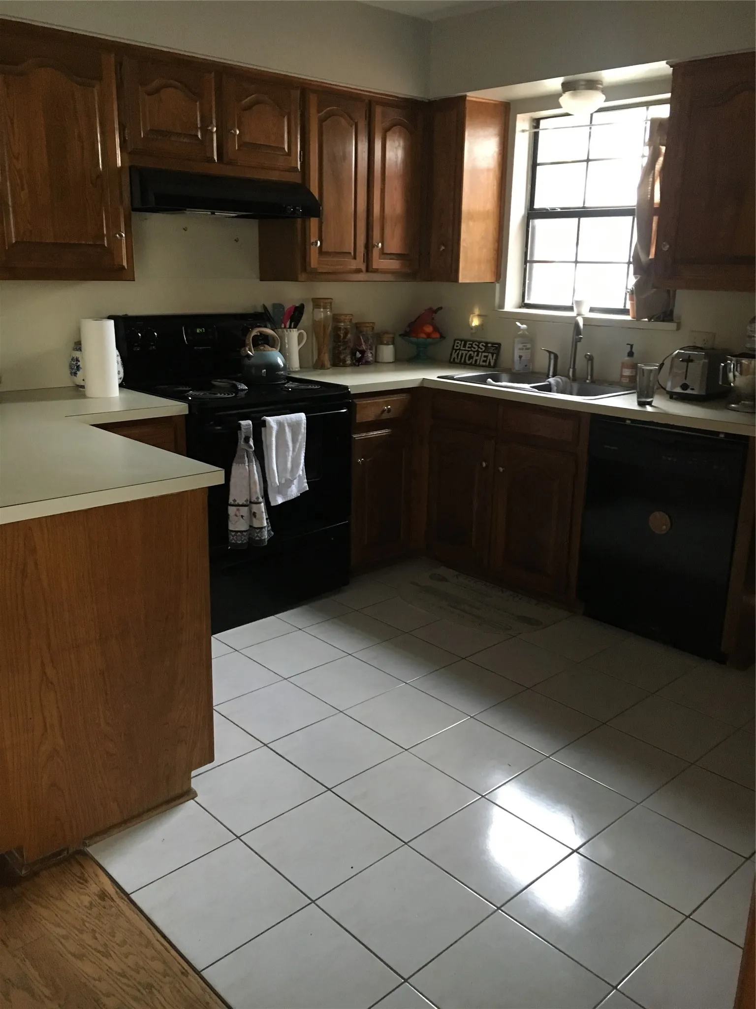 Kitchen featuring wood-finish cabinetry, light-toned countertops, and a black range with an overhead vent