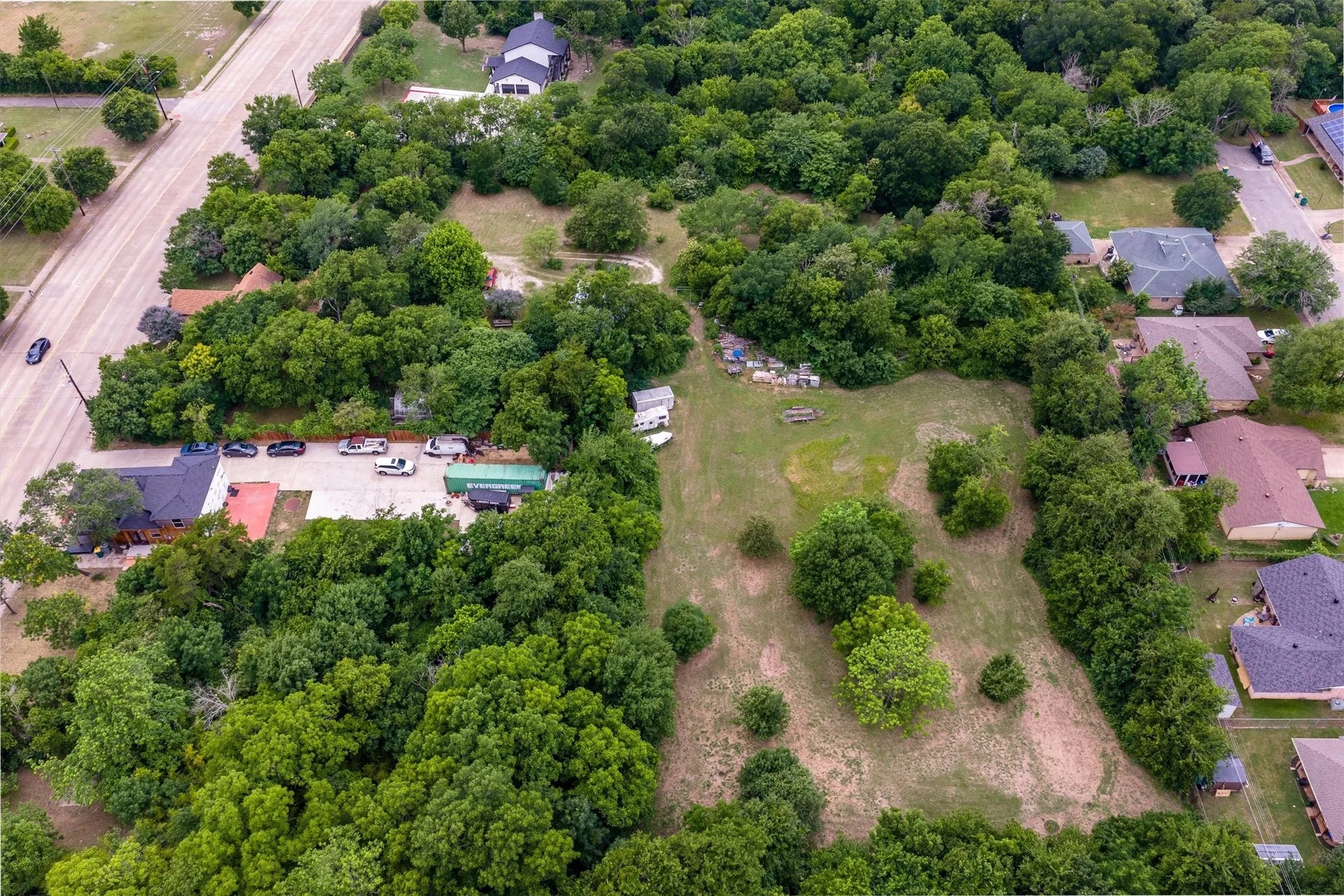 Expansive property featuring mature trees, open grassy areas, and a paved parking lot