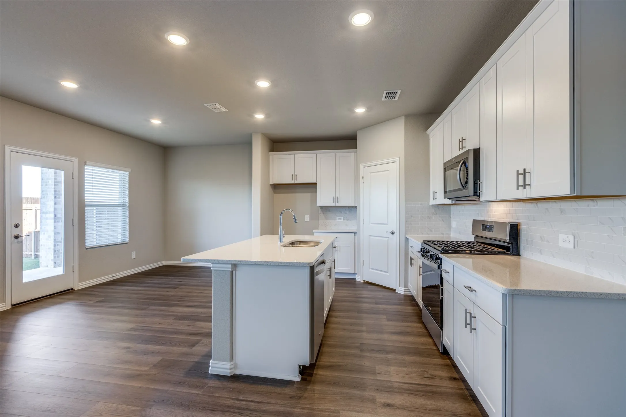 Kitchen with dark hardwood / wood-style floors, sink, white cabinetry, stainless steel appliances, and a center island with sink