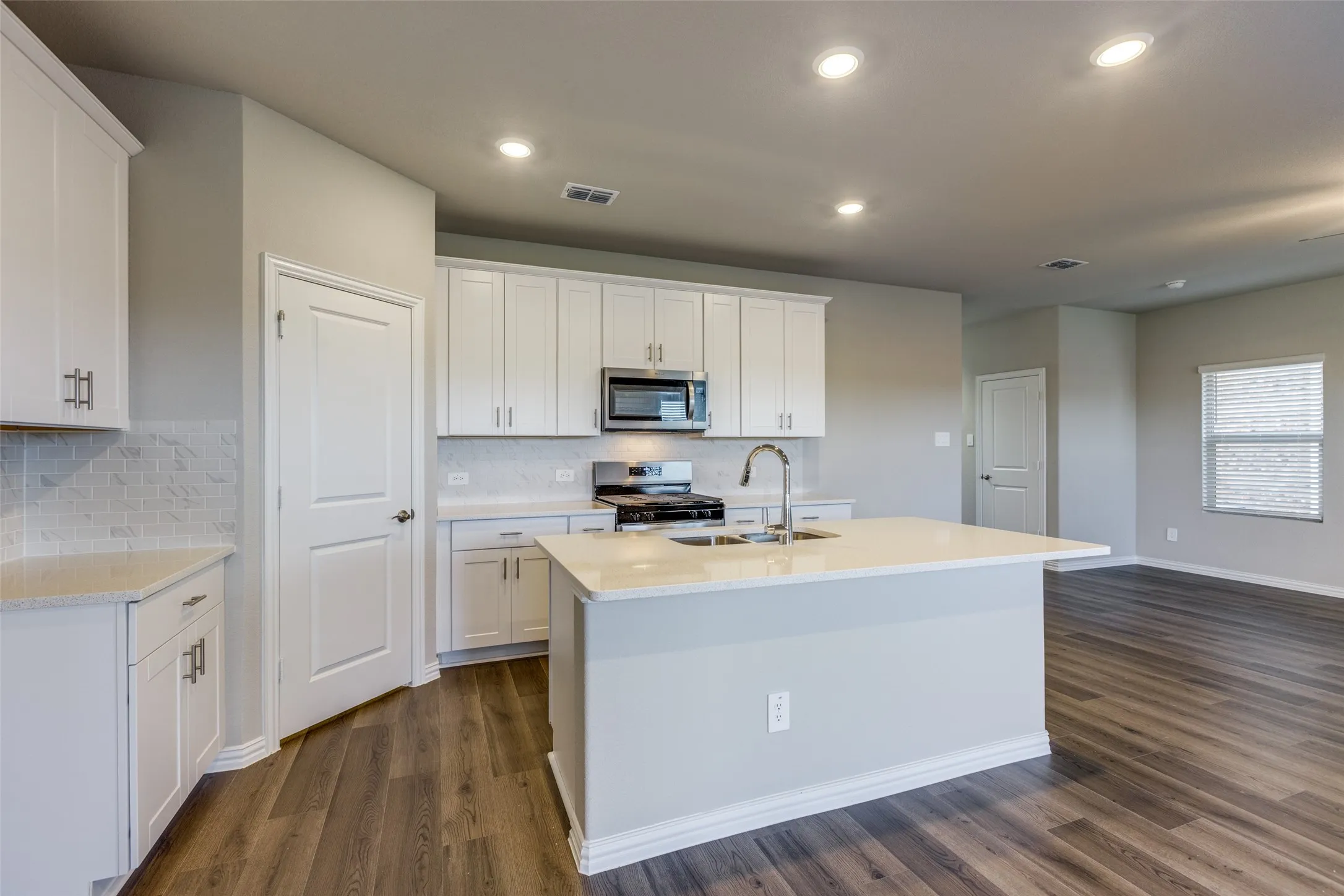 Kitchen featuring dark wood-type flooring, white cabinets, stainless steel appliances, a center island with sink, and sink