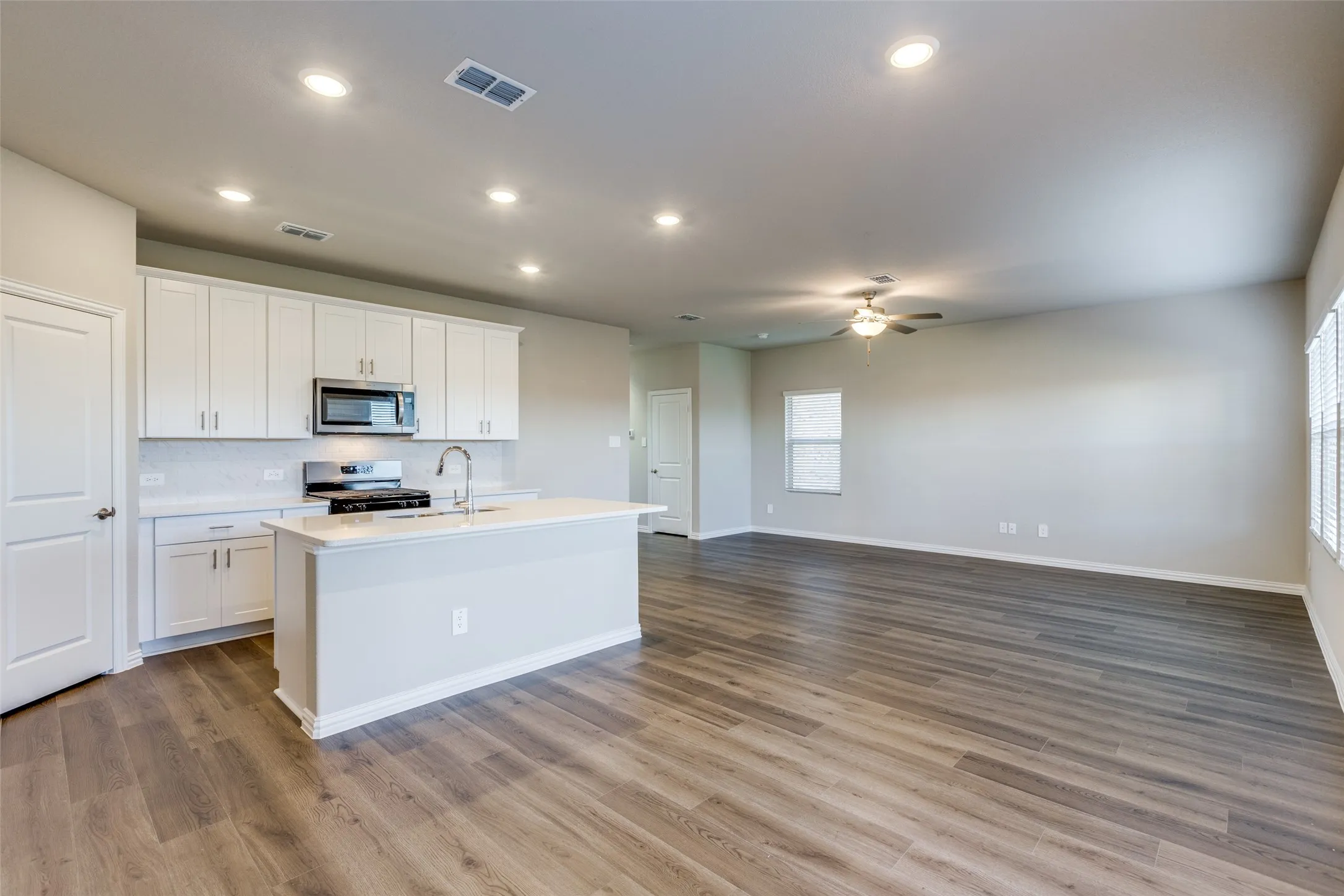 Kitchen with appliances with stainless steel finishes, white cabinetry, ceiling fan, and light hardwood / wood-style flooring